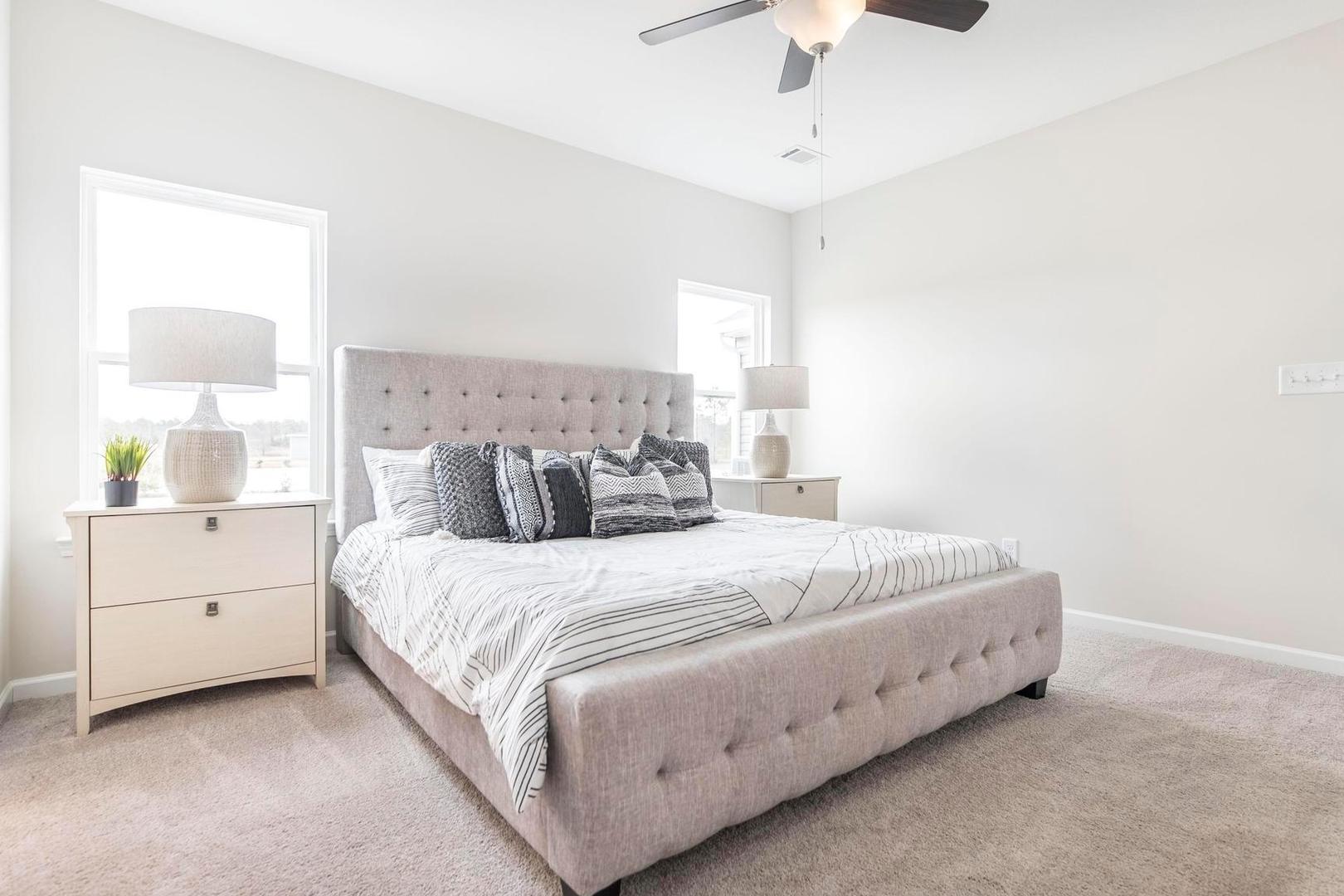 Spacious primary bedroom at Cape Reserve at Donahue Ridge in Auburn Alabama with tufted upholstered bed, ceiling fan and neutral decor