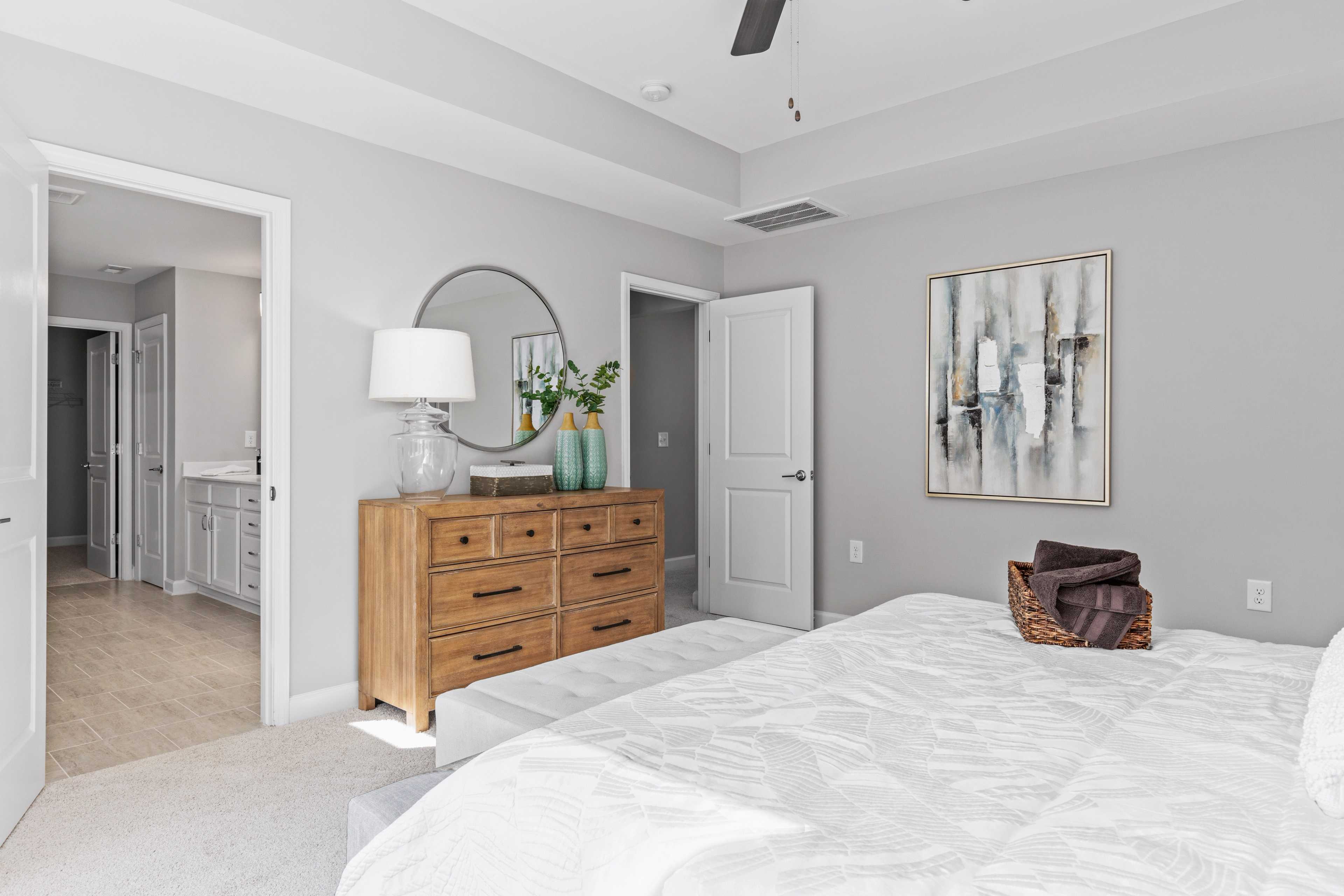 Spacious primary bedroom at Enclave at Belmont in Belmont NC with gray walls, wooden dresser, round mirror, and en-suite bath