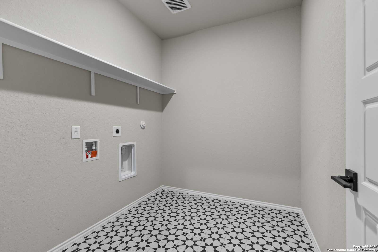 Spacious laundry room with white built-in shelves, washer-dryer hookups, utility sink, and geometric tile floor in Davidson Homes The Murray I, San Antonio