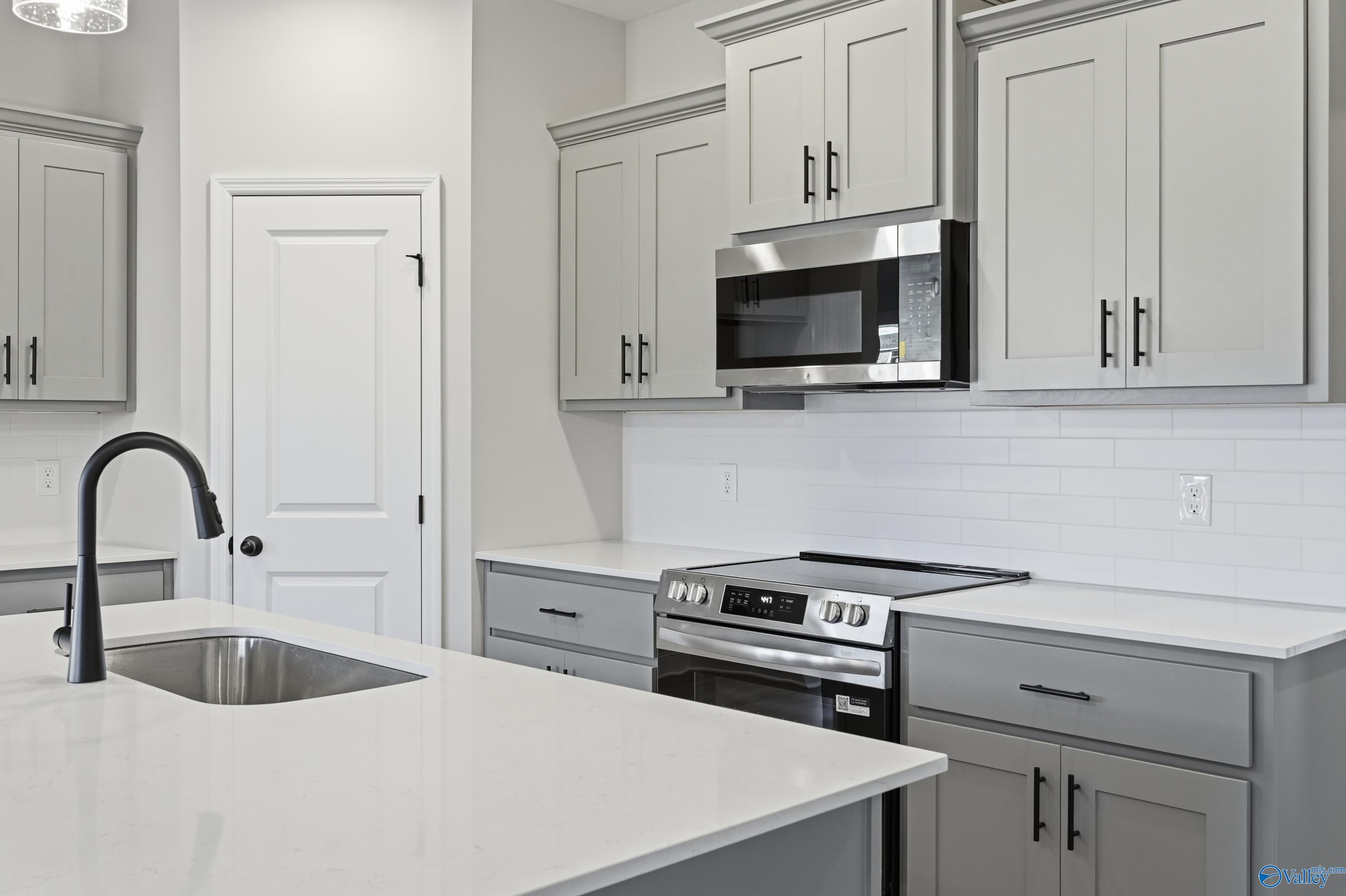Modern white shaker kitchen with stainless appliances, quartz island sink, subway tile backsplash in Davidson Homes The Daphne C, Athens AL