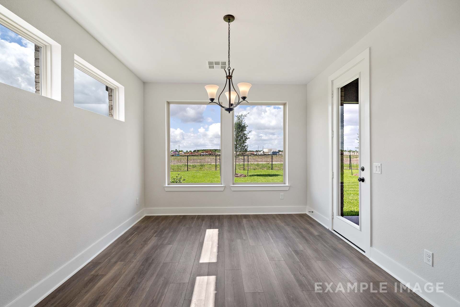 Bright dining room in The Victoria by Davidson Homes with wood-look tile flooring, chandelier, and backyard views.