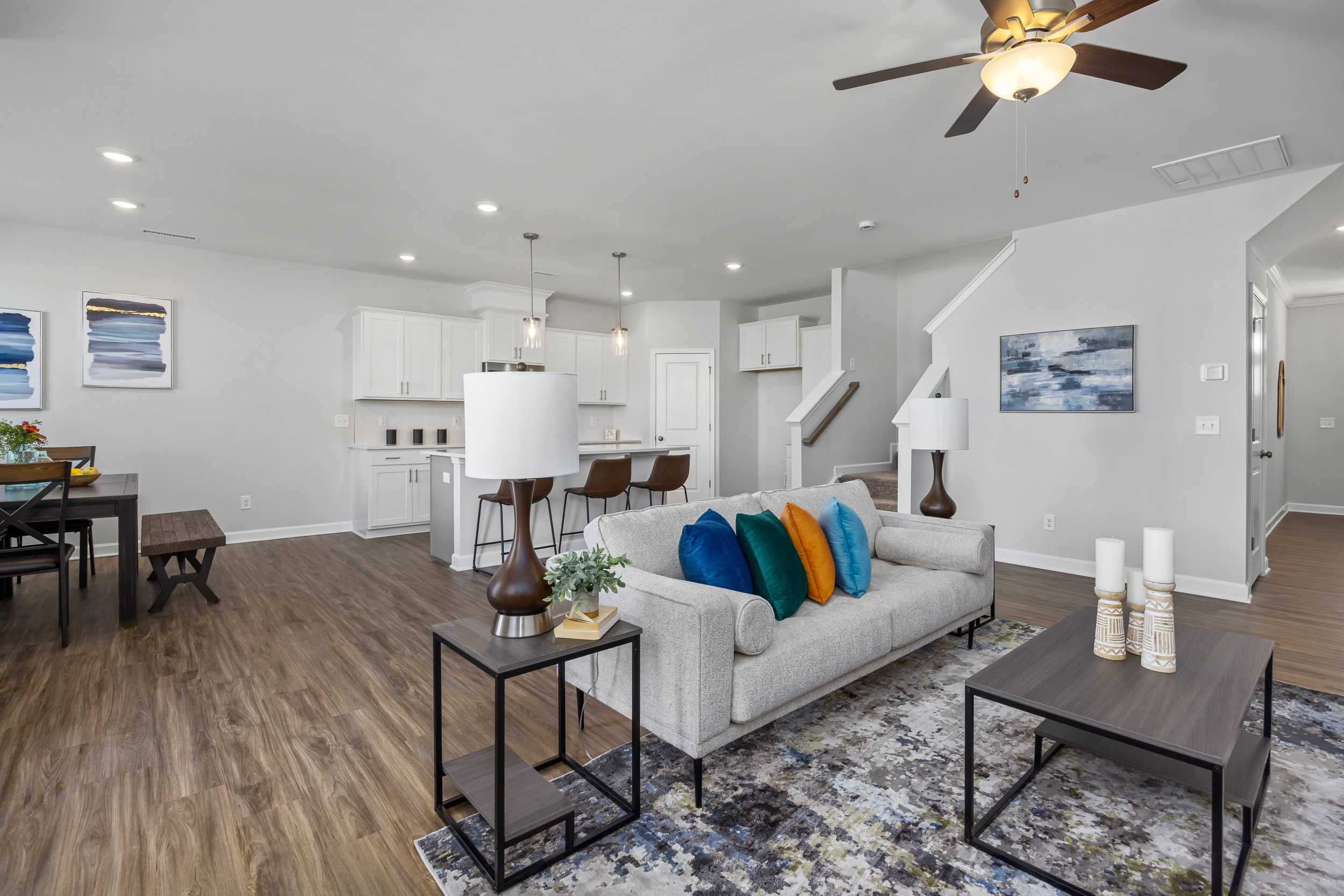 Open-concept living room and kitchen at Woodland Crossing in Zebulon NC with hardwood floors, gray sofa, colorful pillows, and modern island