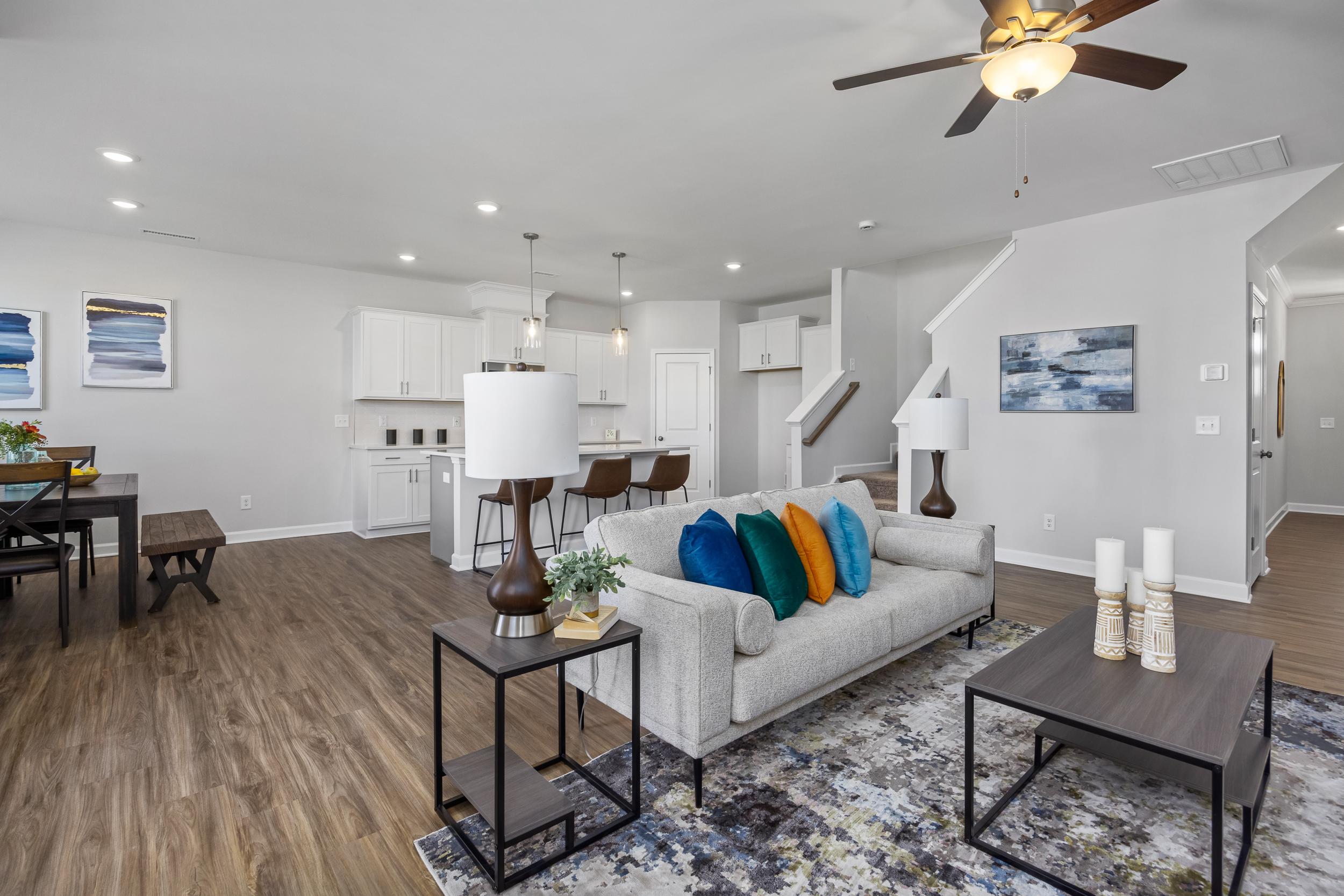 Open-concept living room and kitchen at Woodland Crossing in Zebulon NC with hardwood floors, gray sofa, colorful pillows, and modern island