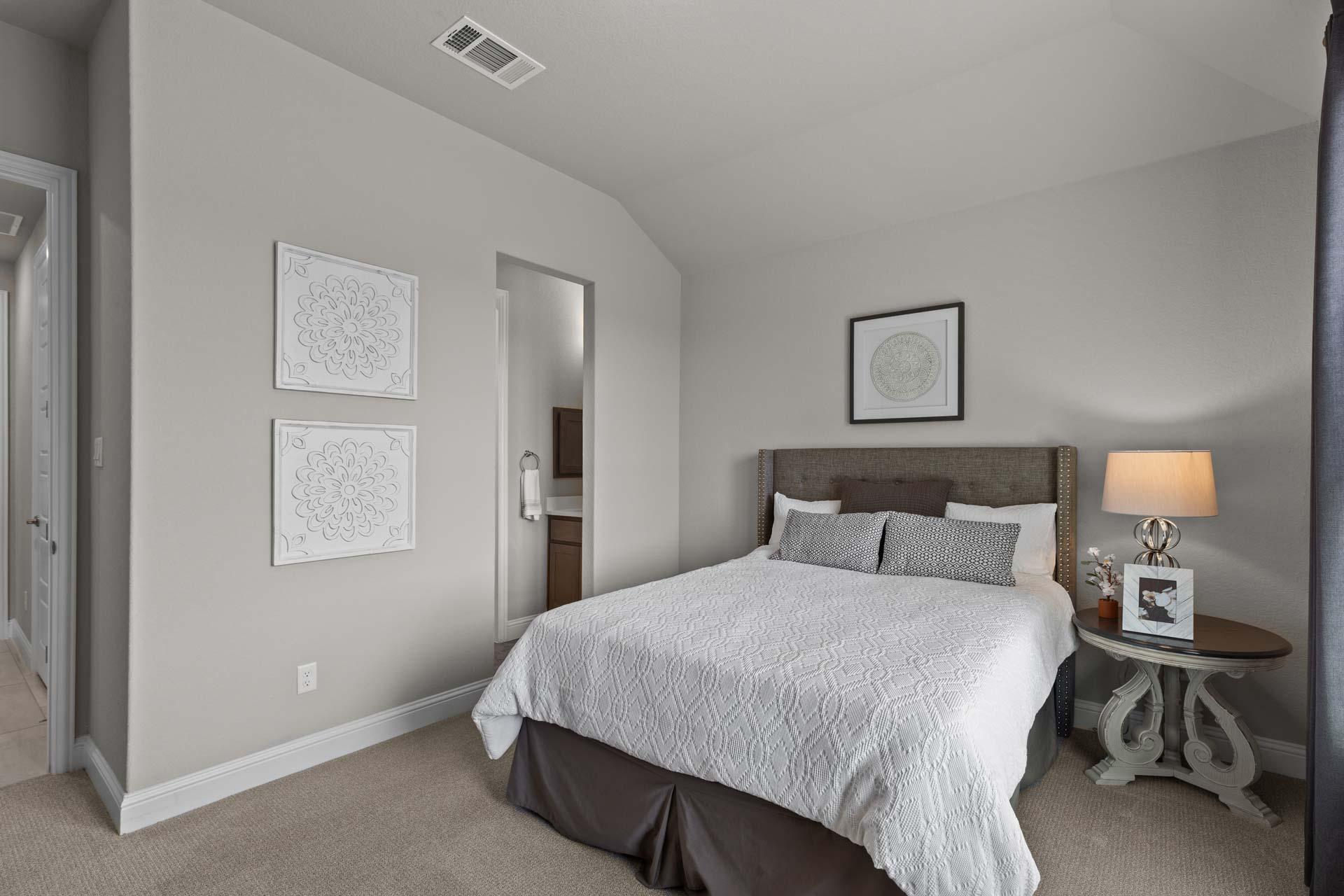 Cozy secondary bedroom in The Garner A with queen bed, gray walls, tufted headboard, bedside lamp, and en-suite bath