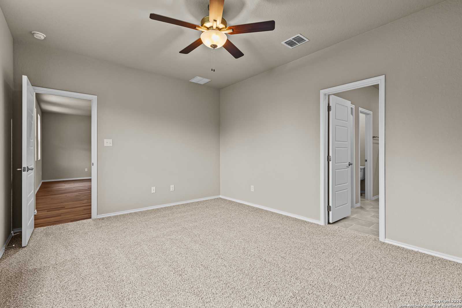 Spacious secondary bedroom with beige carpet, ceiling fan, and doors to bath and hallway in Davidson Homes The Douglas F, San Antonio