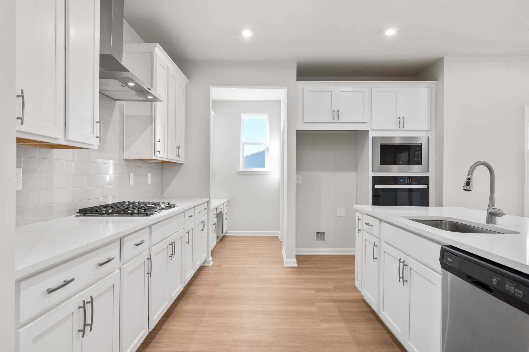 Spacious modern kitchen in The Dawson A featuring white shaker cabinets, stainless steel appliances, large island, and light oak floors