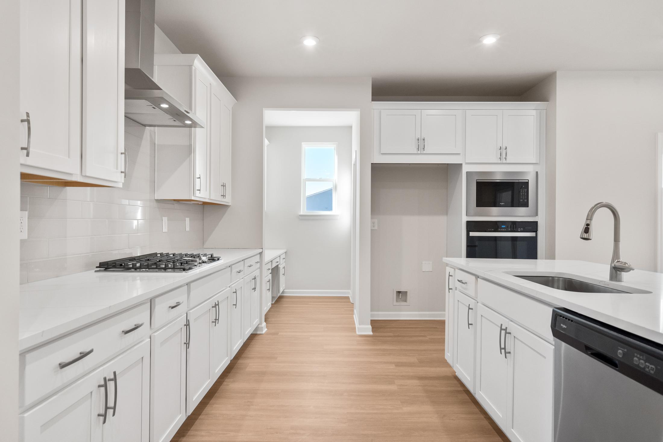 Spacious modern kitchen in The Dawson B with white shaker cabinets, large island sink, gas cooktop, and stainless steel appliances