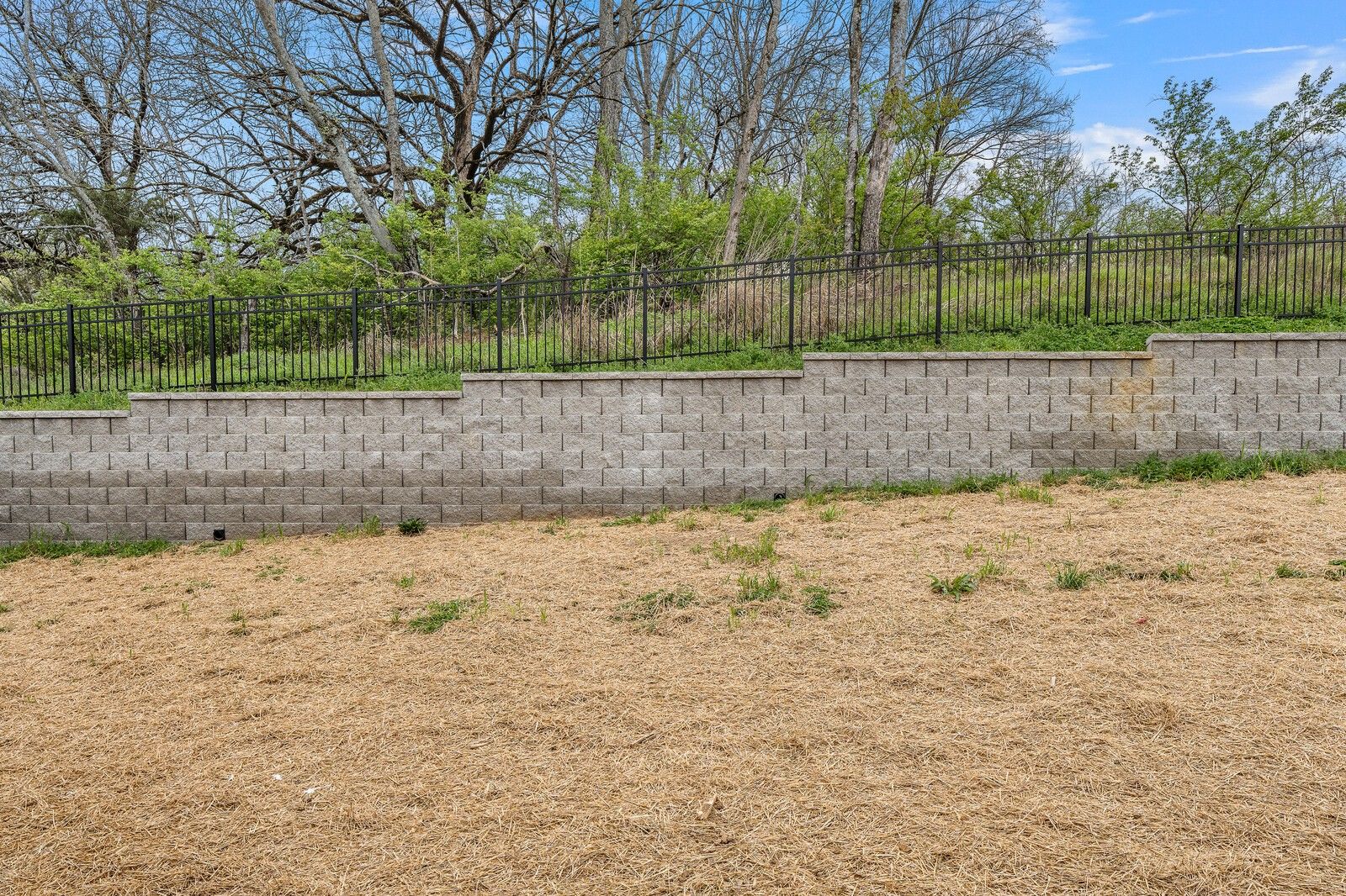 Sturdy concrete block retaining walls with black metal fence and lush greenery in Woods Crossing backyard, Gallatin, Tennessee