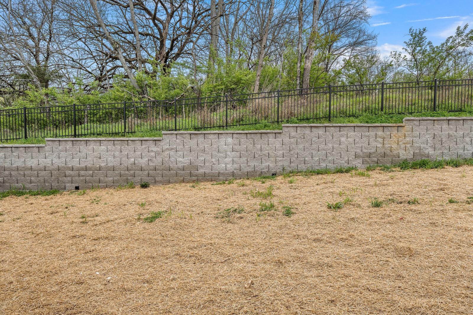 Sturdy concrete block retaining walls with black metal fence and lush greenery in Woods Crossing backyard, Gallatin, Tennessee