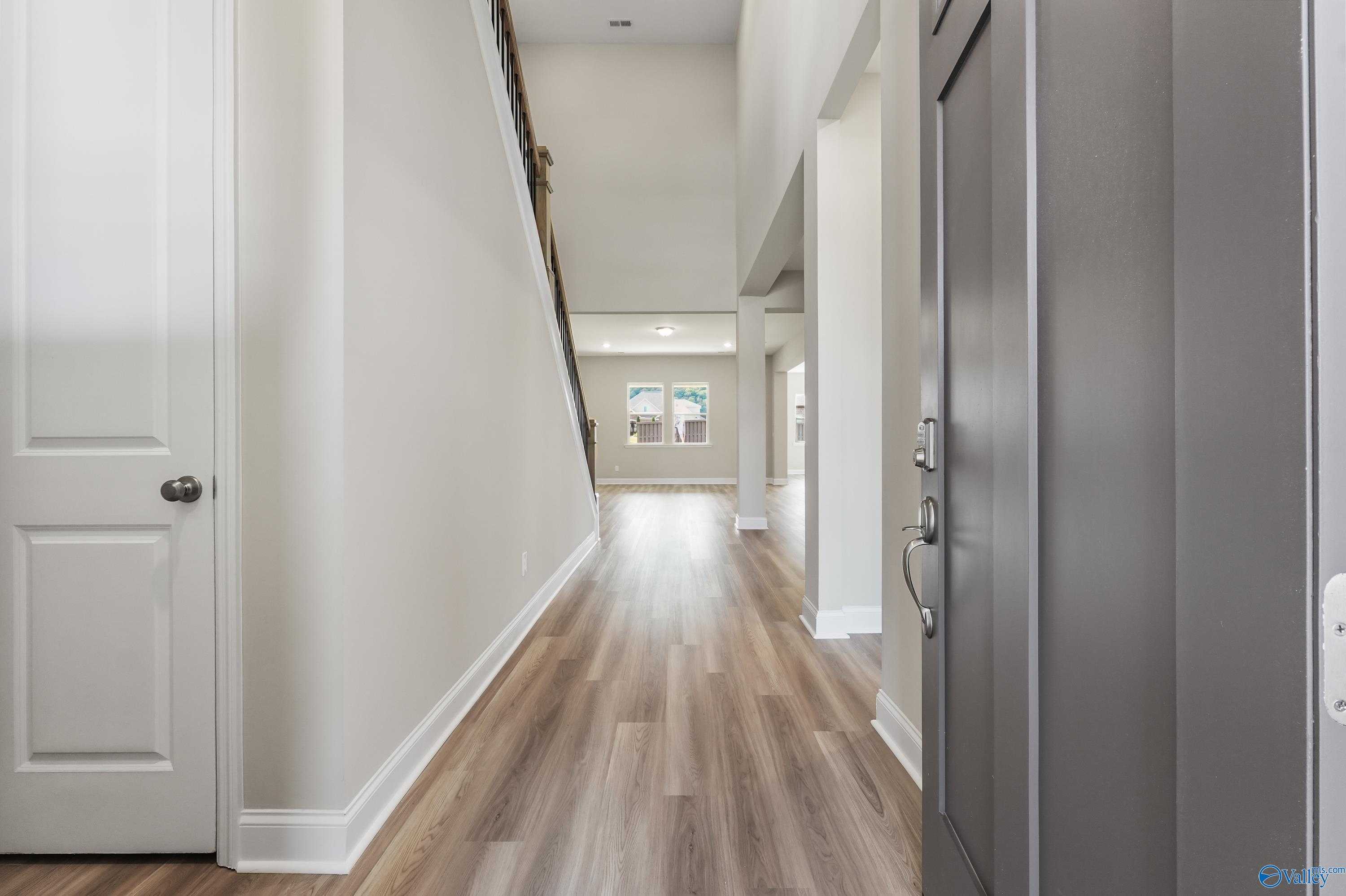 Elegant two-story foyer with grand wooden staircase, hardwood floors, and white walls in Evermore Homes The Haven, Owens Cross Roads, AL