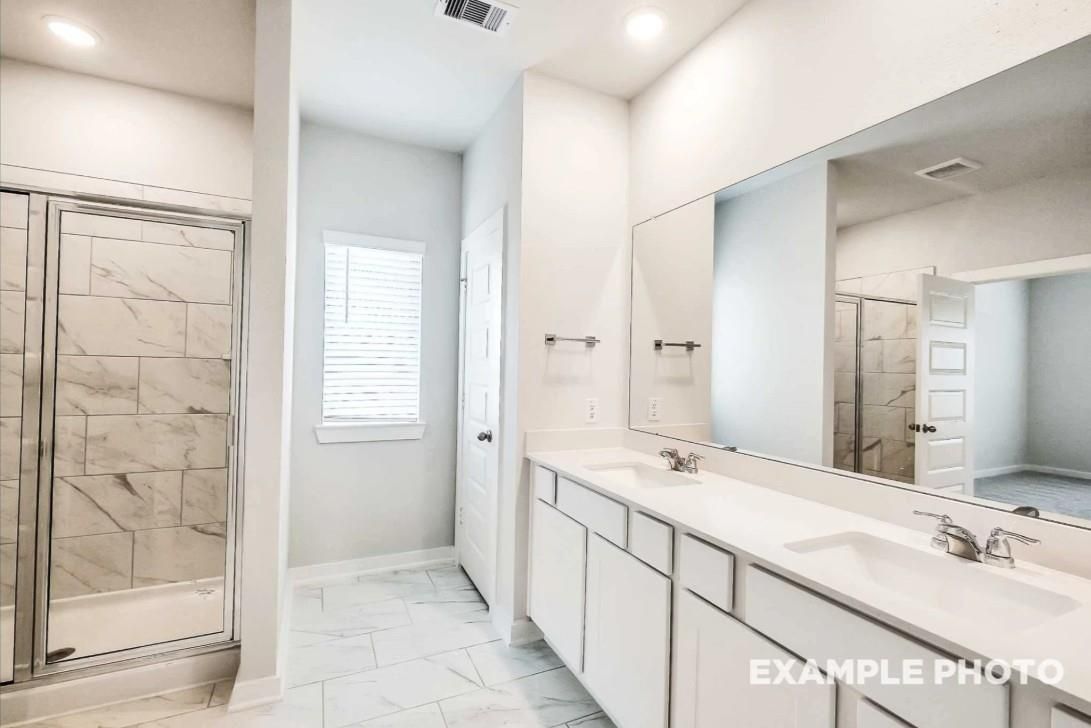 Modern master bathroom with double vanity, large mirror, and marble-tiled glass shower in Davidson Homes The Riviera C, Dayton, Texas