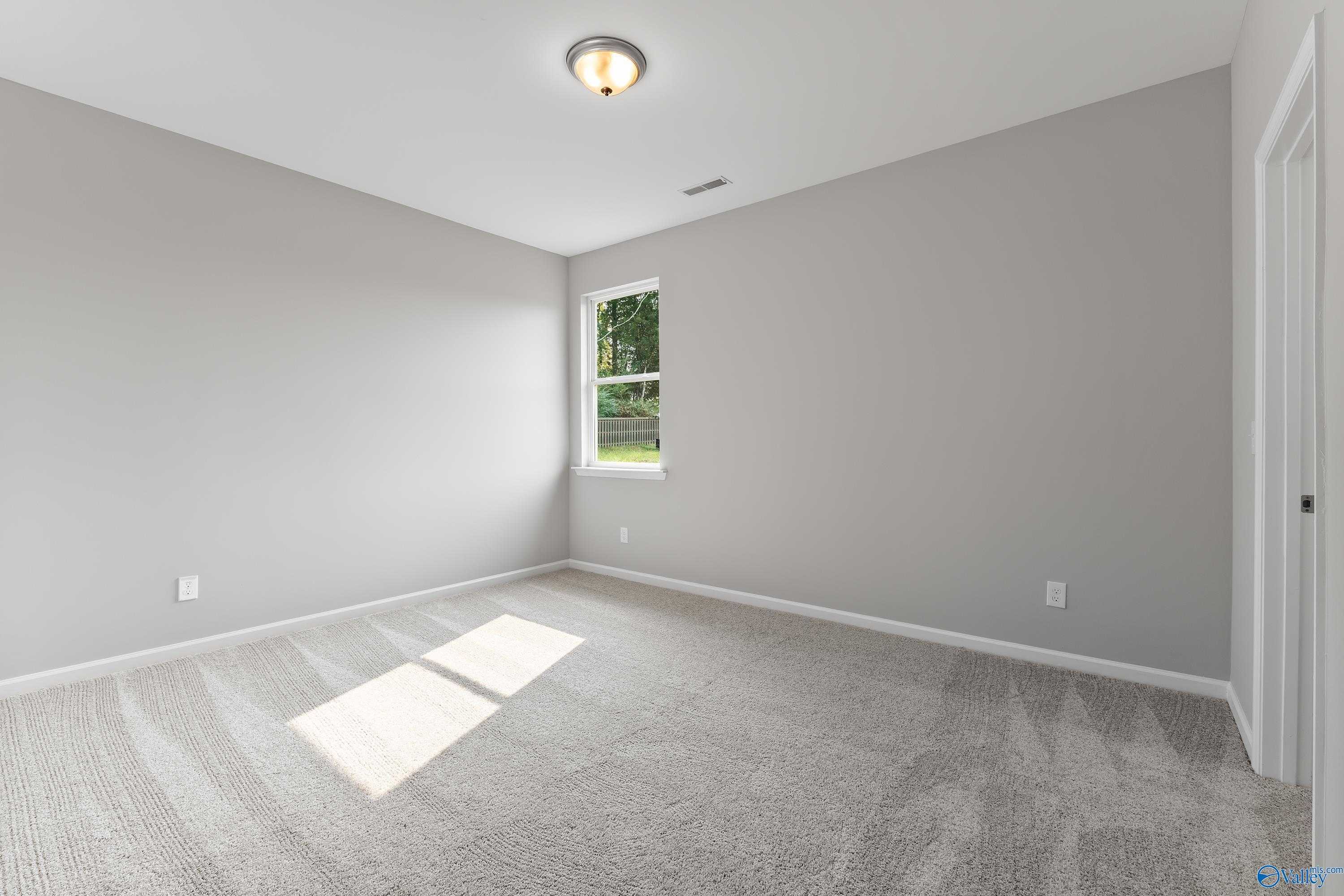 Bright bedroom with gray walls, plush carpet, and large window with tree view in Evermore Homes The Grace, Madison, Alabama