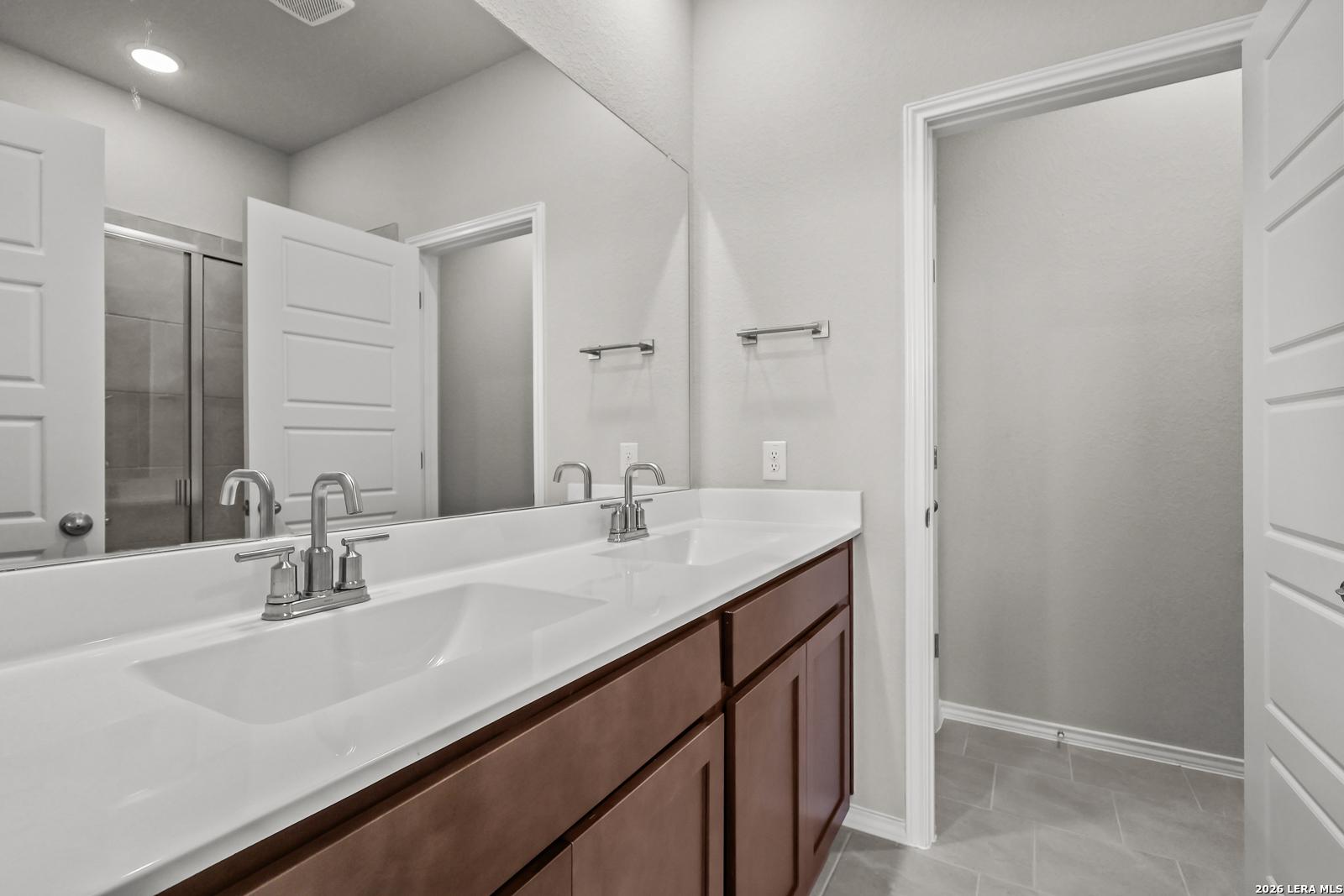 Modern master bathroom featuring double vanity with sinks, large mirror, and glass shower in Davidson Homes The Frio B, San Antonio