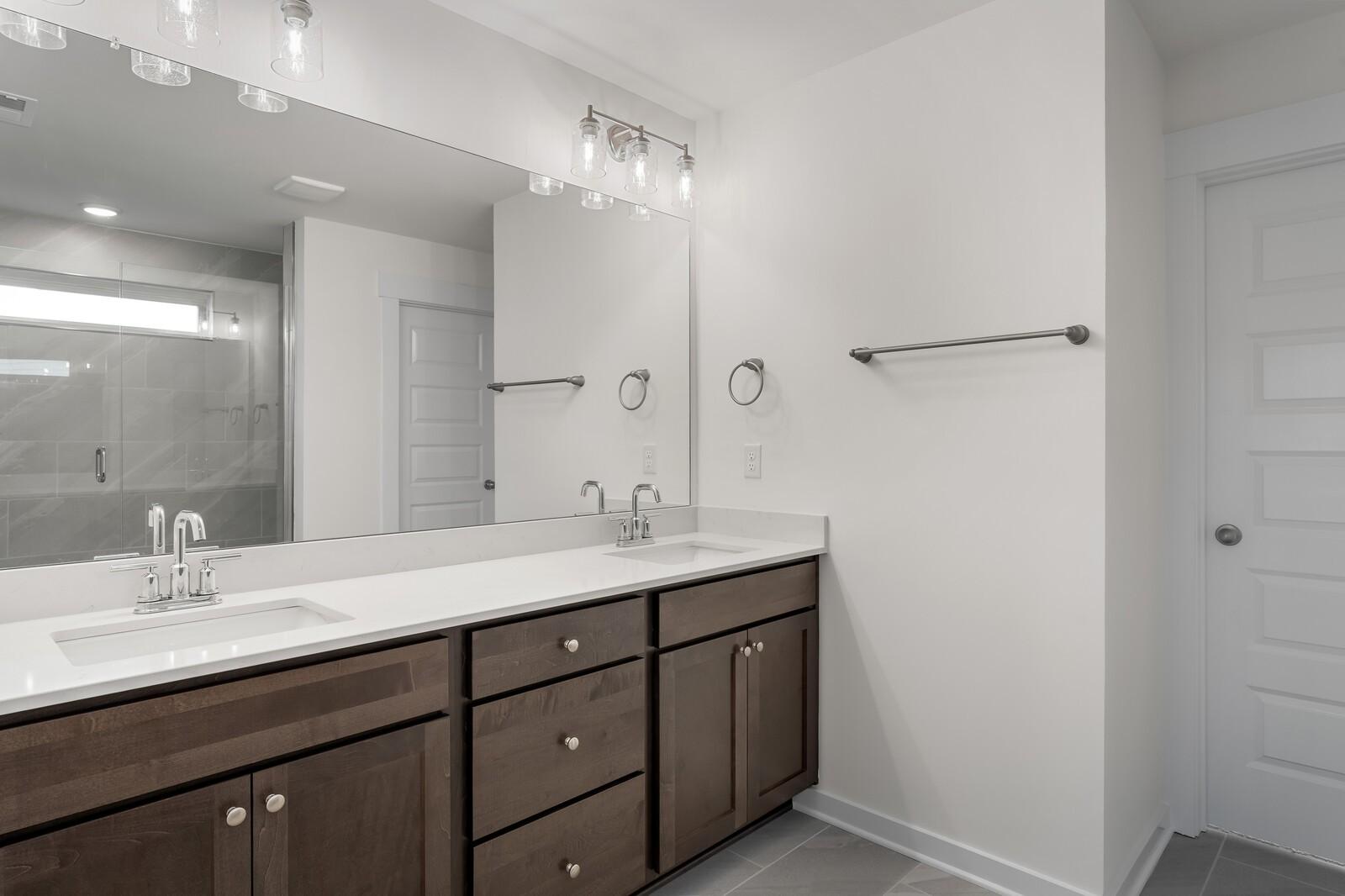 Modern master bathroom with double quartz vanity, dark wood cabinets, large mirror, and glass shower in Davidson Homes The Willow C, Gallatin, TN
