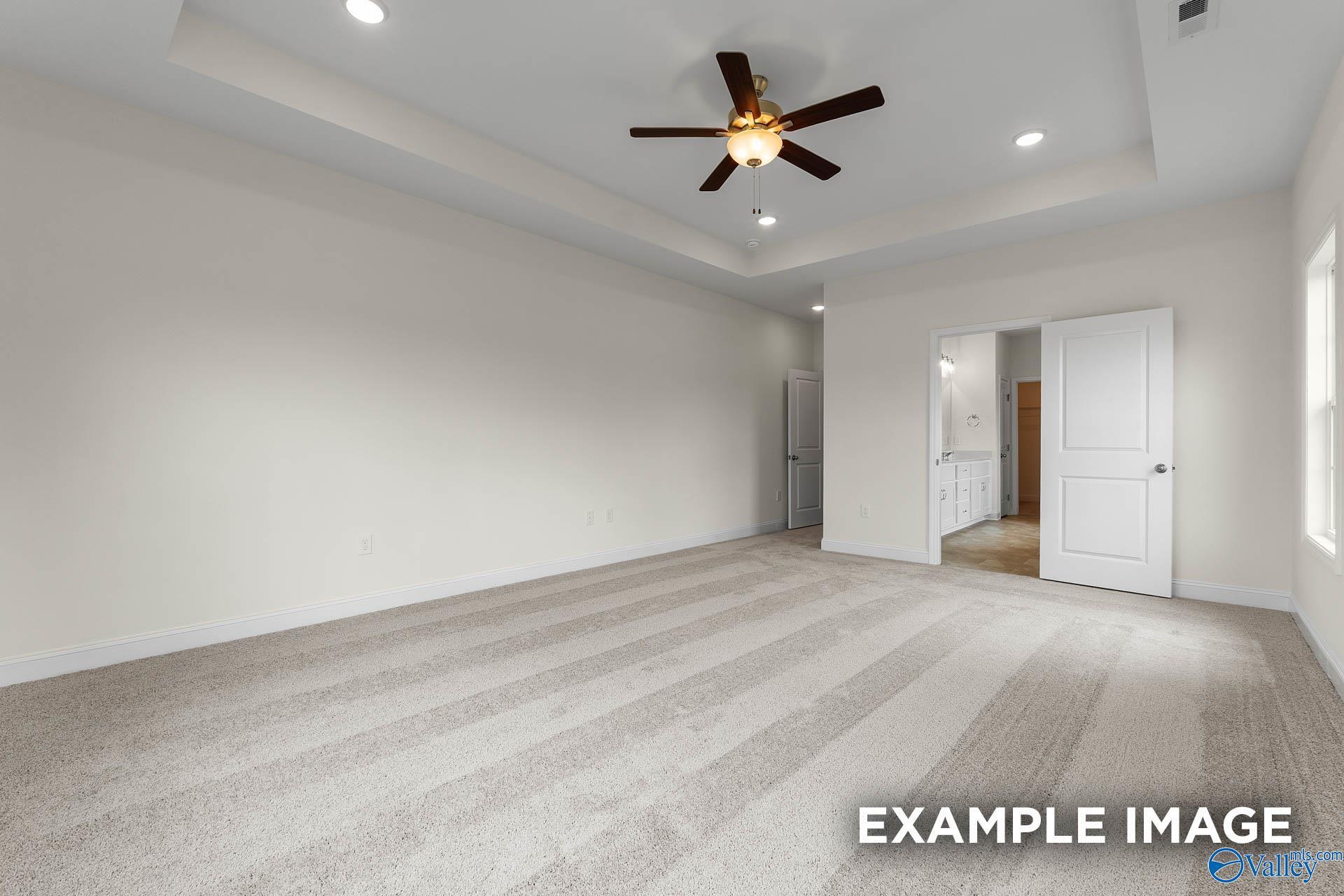 Spacious living room with tray ceiling, ceiling fan, beige carpet, and open kitchen doorway in Davidson Homes The Emory, Toney, Alabama