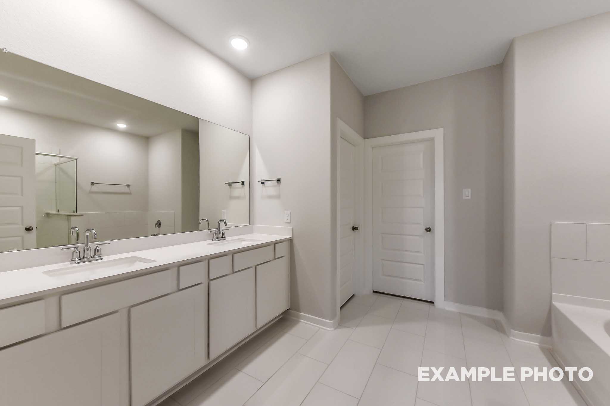 Spacious master bathroom in The Laguna B with double vanity, large mirror, and freestanding tub