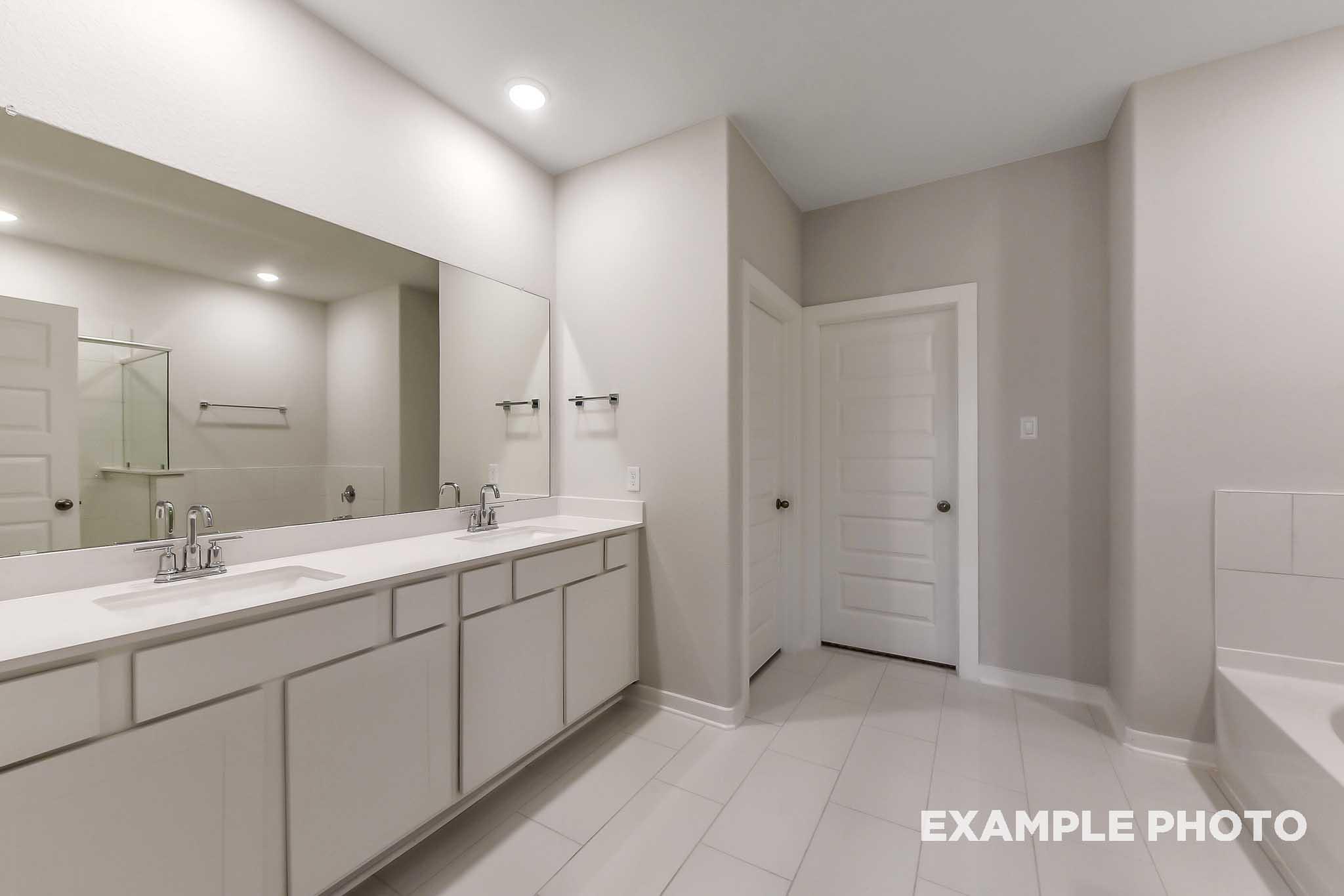 Spacious master bathroom in The Laguna B with double vanity, large mirror, and freestanding tub