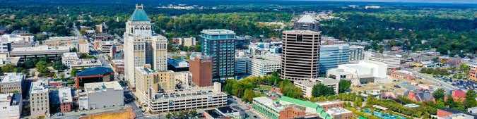 Aerial view of Greensboro skyline with towering downtown buildings, urban streets, and green outskirts