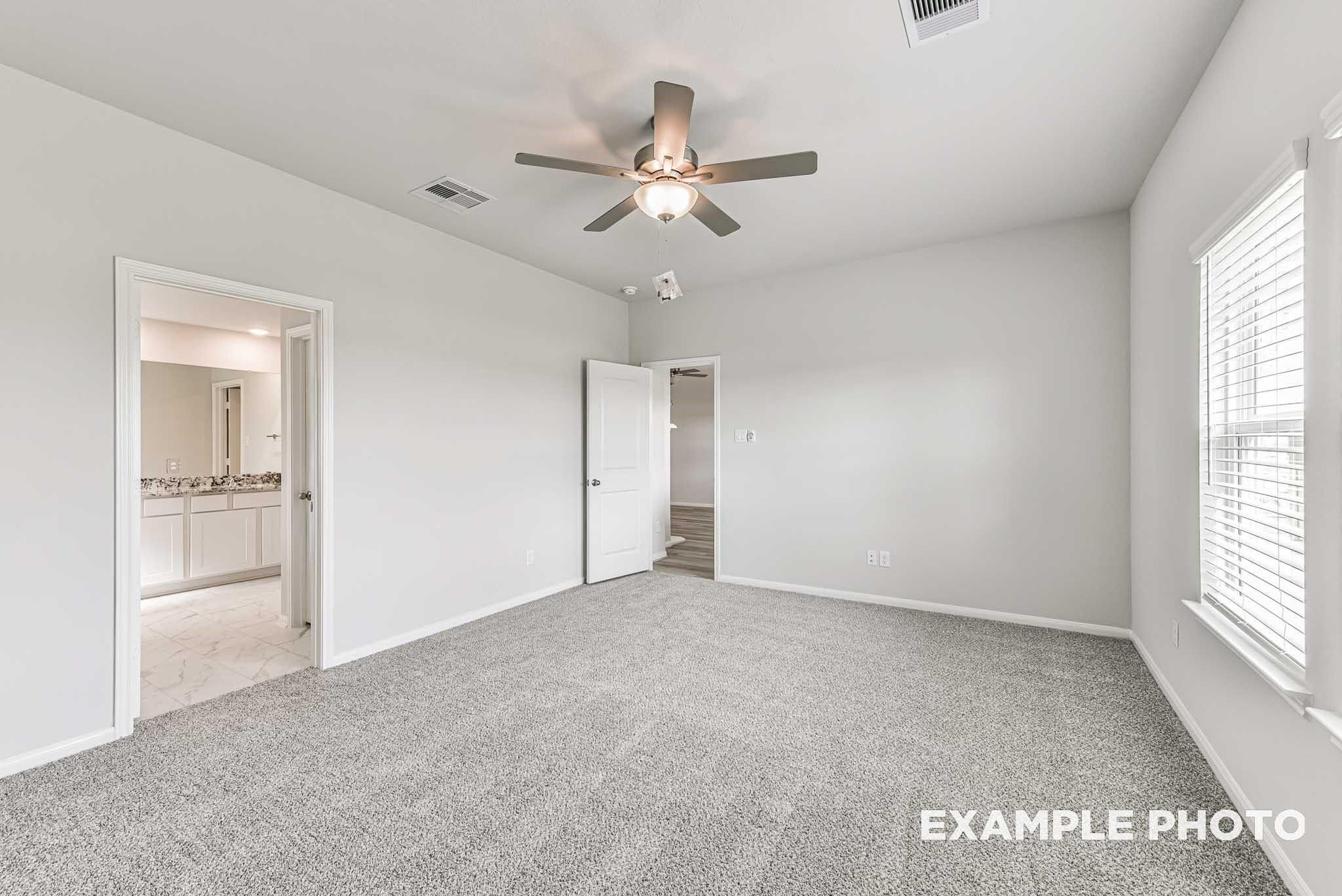 Spacious bedroom with gray carpet, ceiling fan, and en-suite bathroom in Davidson Homes The Riviera A, Rosharon, Texas