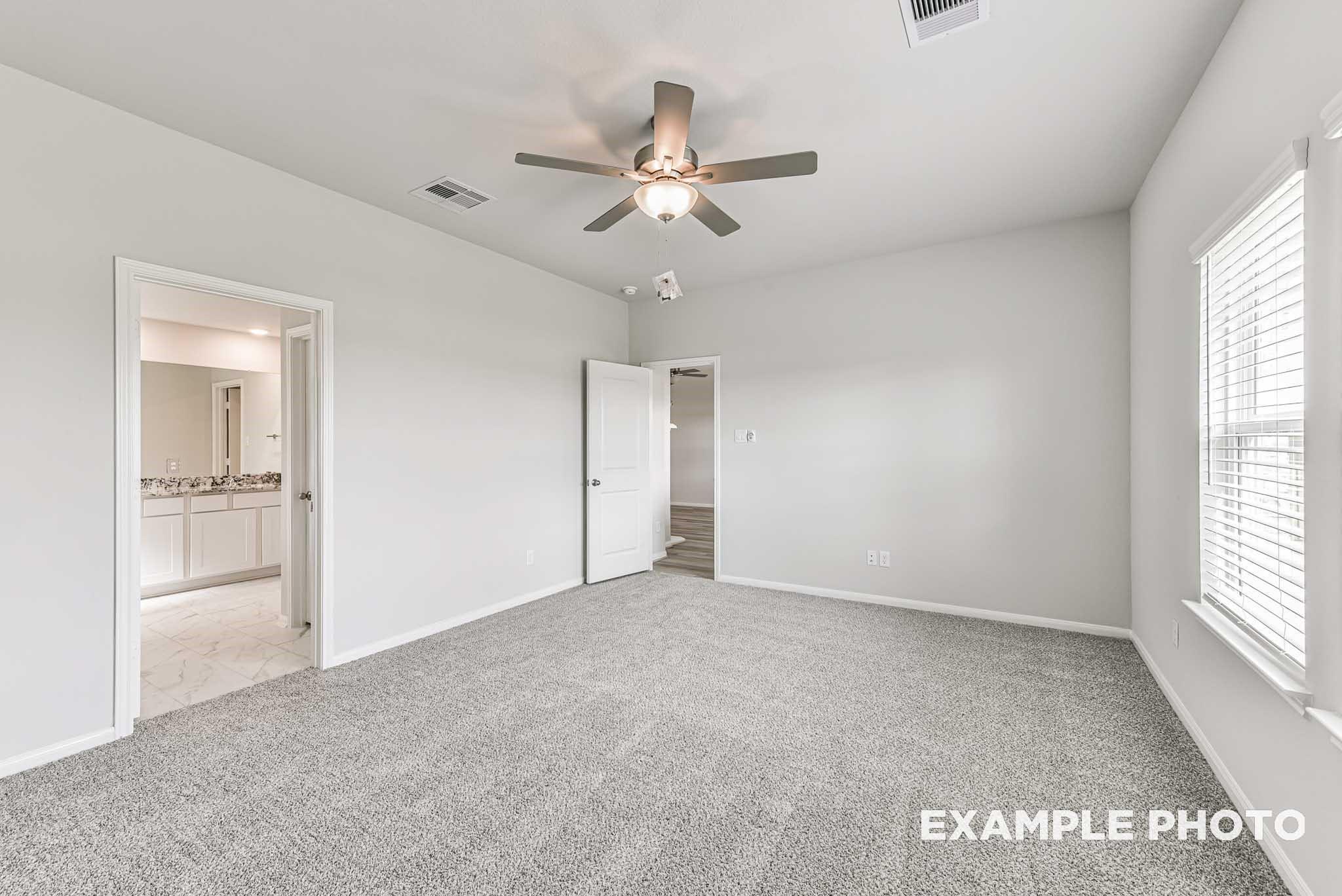 Spacious bedroom with gray carpet, ceiling fan, and en-suite bathroom in Davidson Homes The Riviera A, Rosharon, Texas