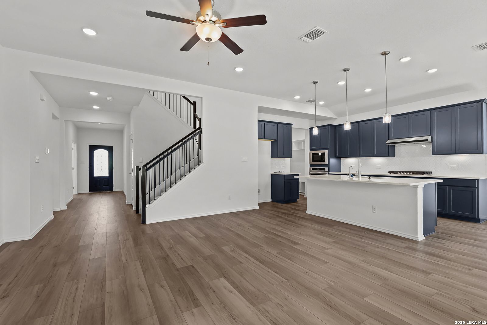 Open foyer with black staircase, navy cabinets, white island, and hardwood floors in Davidson Homes The Sequoia B, Comanche Ridge, San Antonio