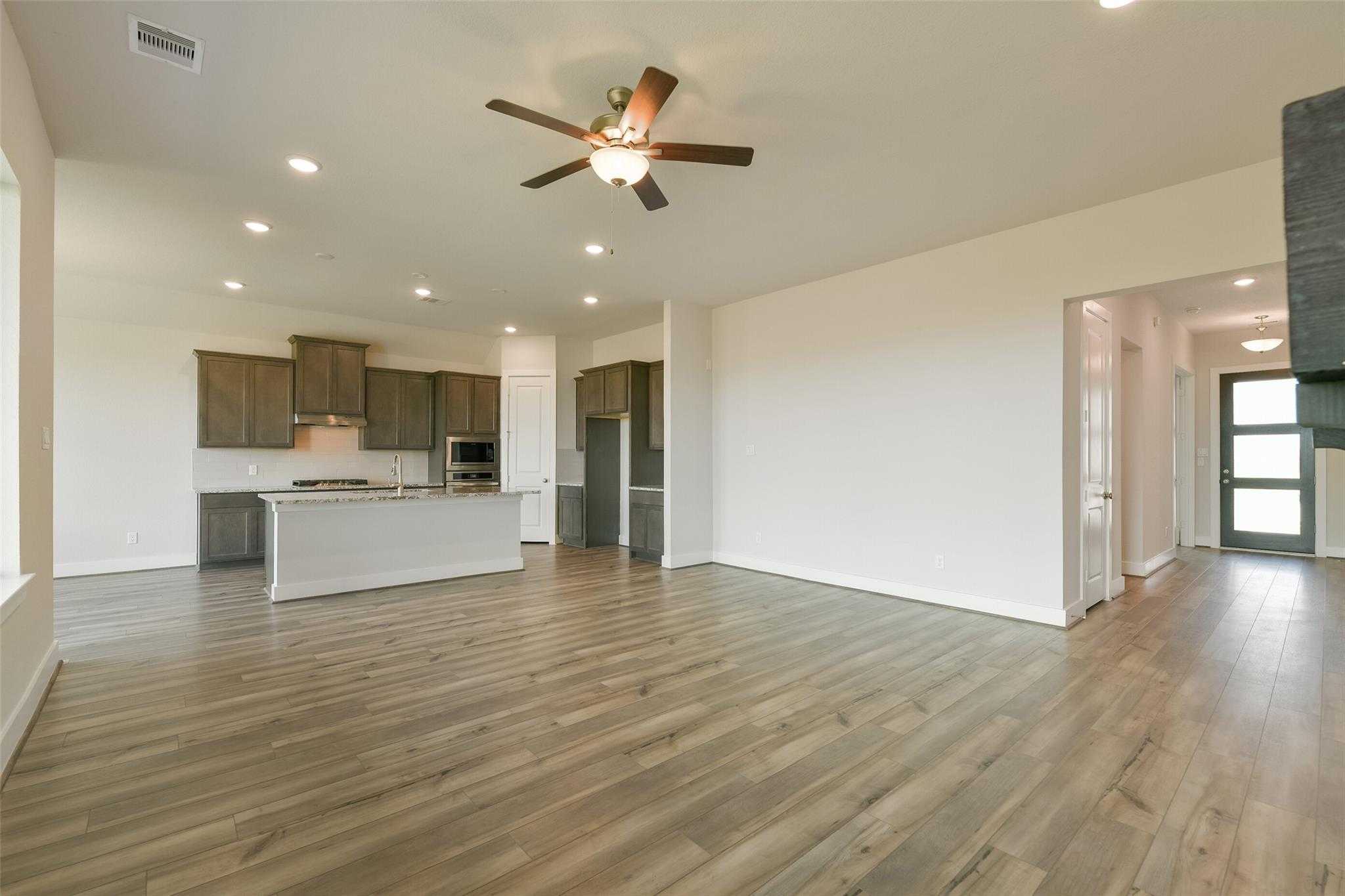 Open-concept living and kitchen with hardwood floors, white island, stainless appliances, ceiling fan in Davidson Homes The Edward A, Lago Mar, Texas City
