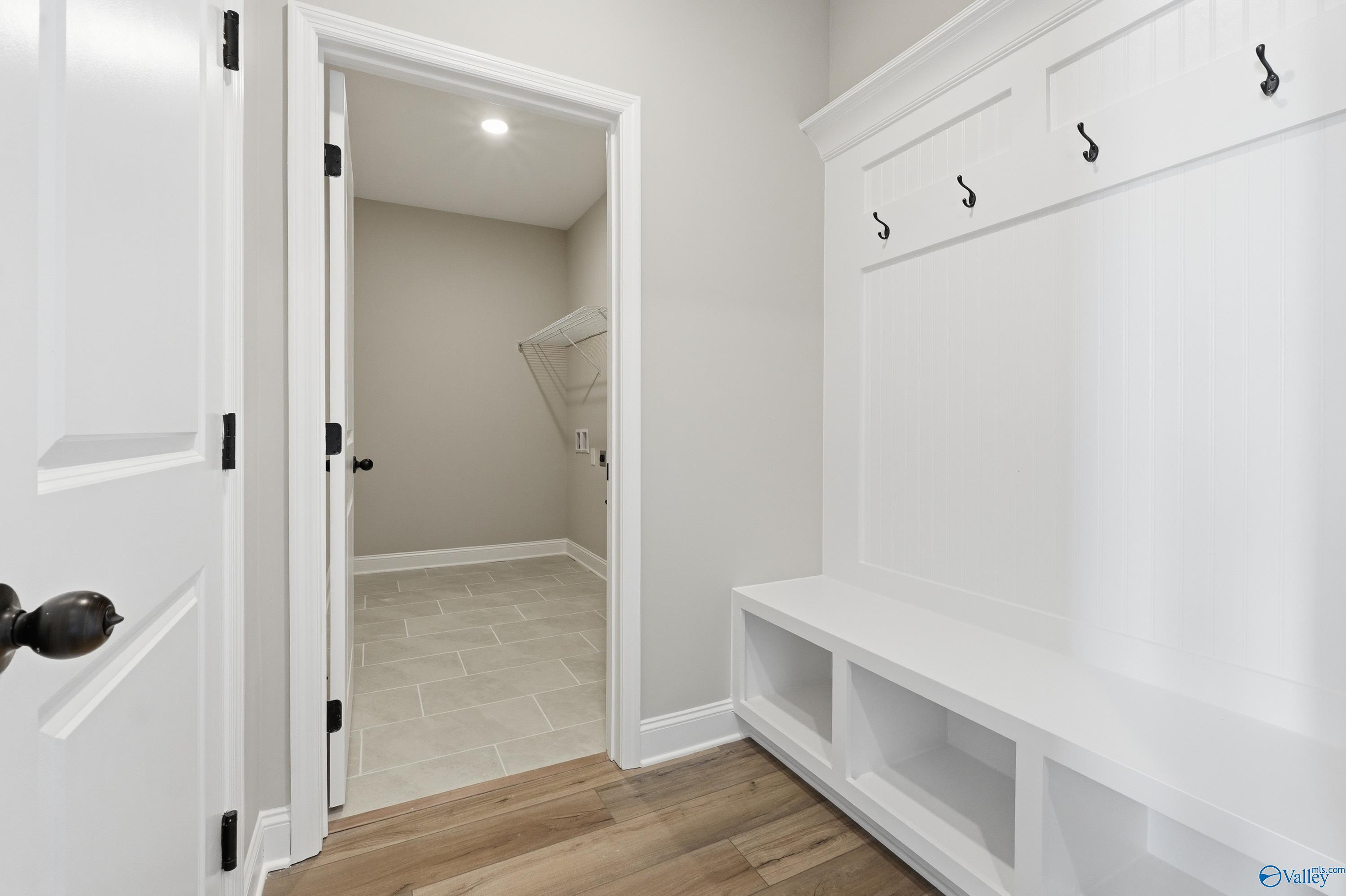White mudroom cabinet with coat hooks, bench, and open laundry room in Davidson Homes The Rockford, Creekside, Harvest, AL
