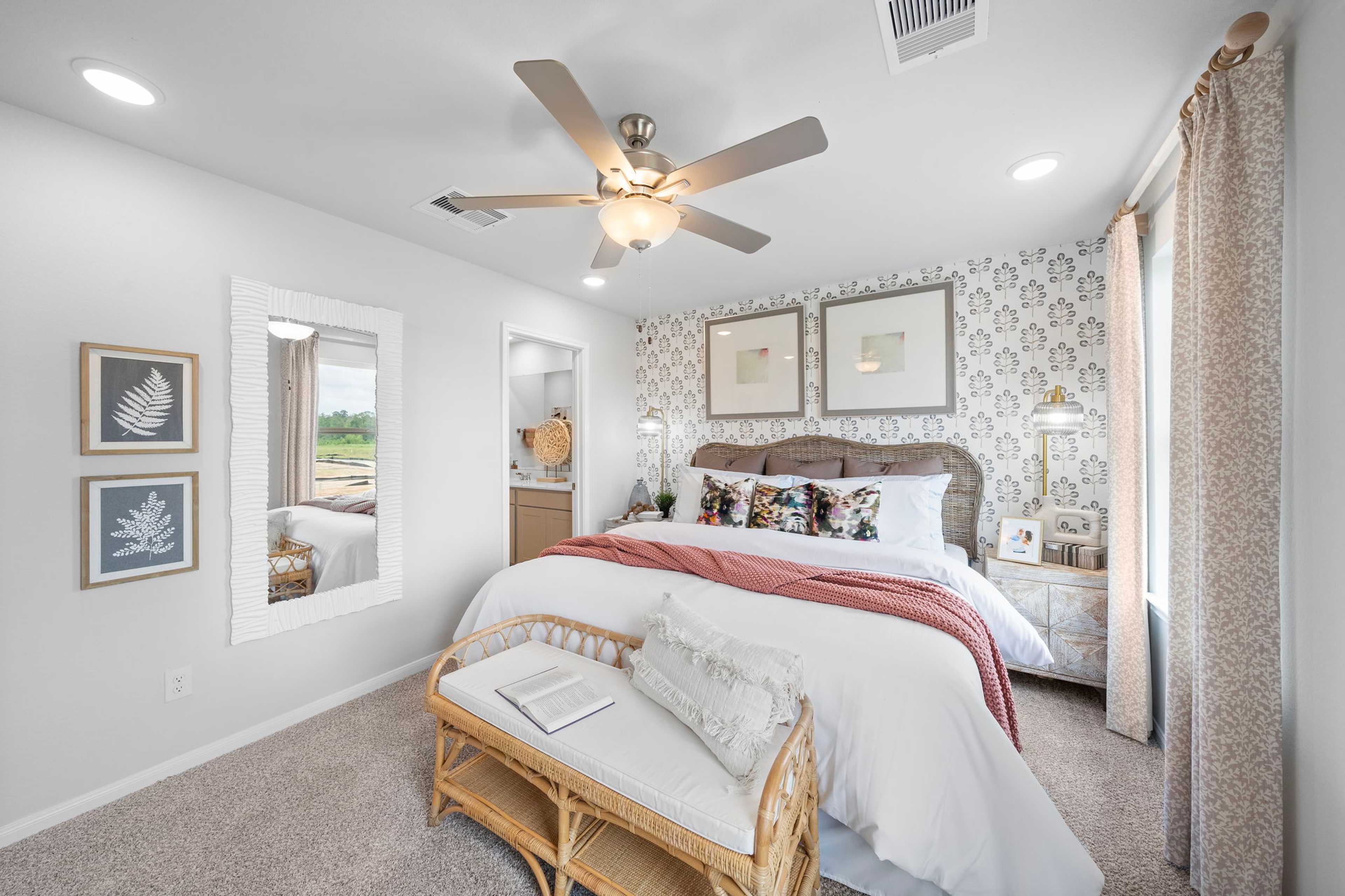 Spacious primary bedroom at Spring Branch Crossing in Conroe Texas with king bed, rattan bench, ceiling fan, and botanical wall art