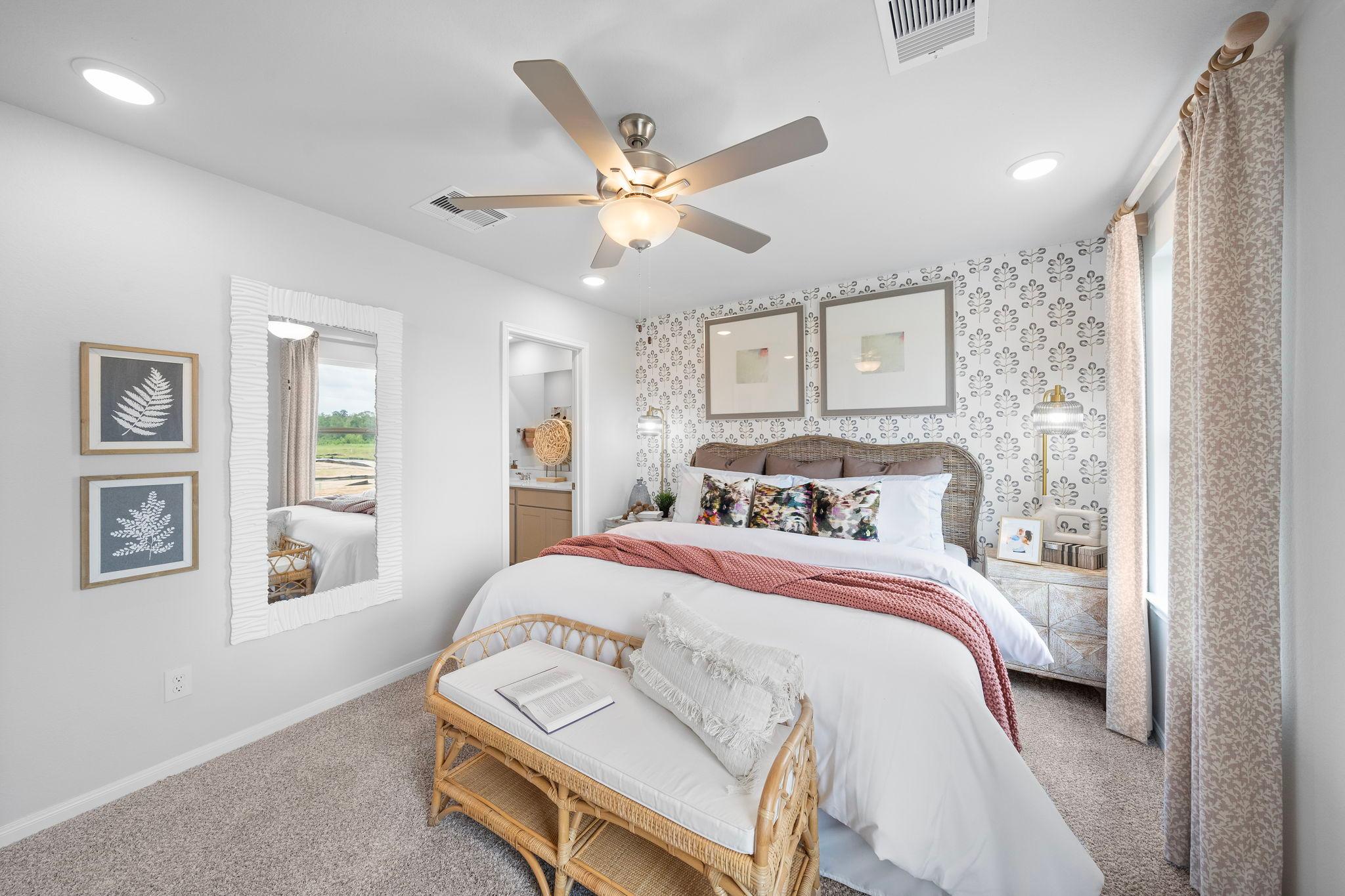 Spacious primary bedroom at Spring Branch Crossing in Conroe Texas with king bed, rattan bench, ceiling fan, and botanical wall art