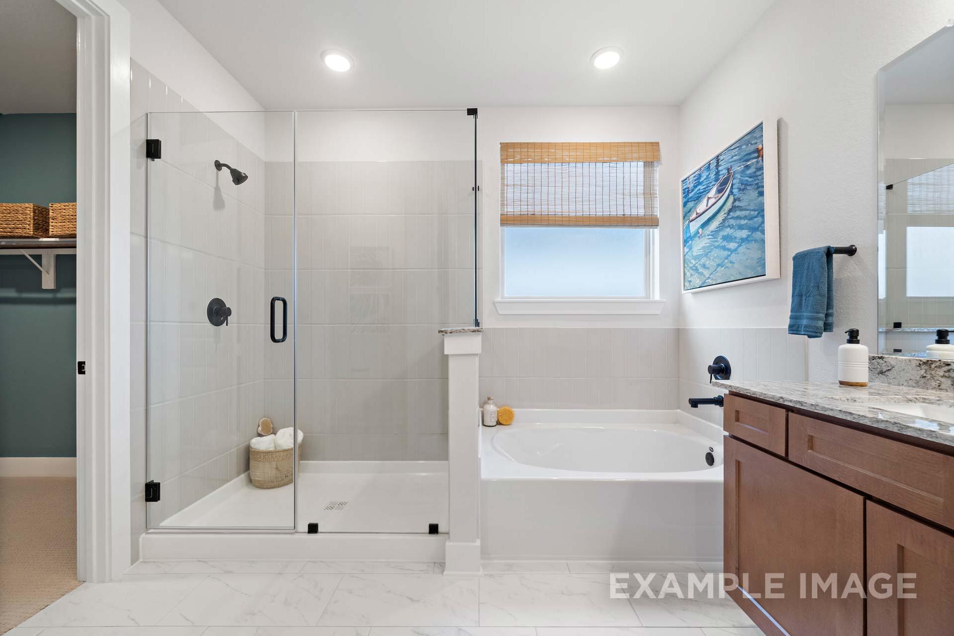 Spacious master bathroom in The Edward A featuring frameless glass shower, soaking tub, and double vanity