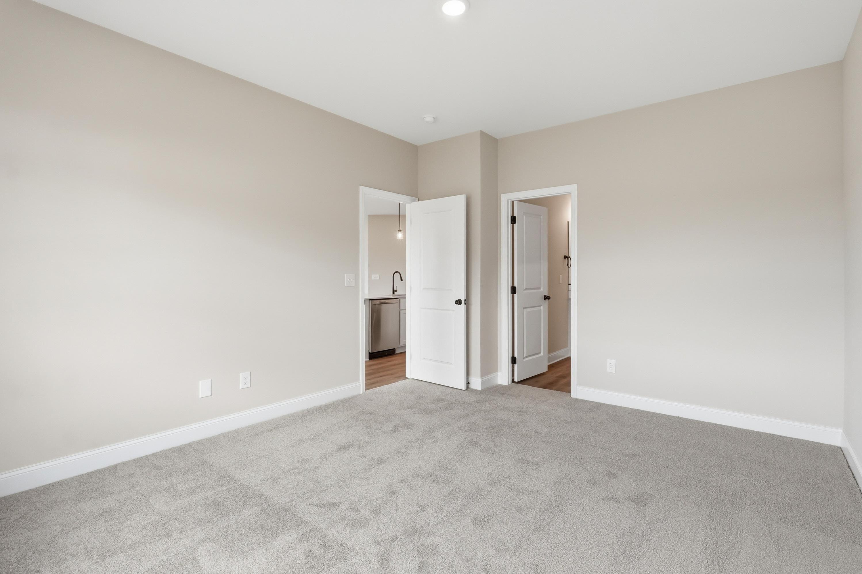 Spacious bedroom in The Glen A model featuring plush carpeting and neutral walls with views into adjacent rooms.