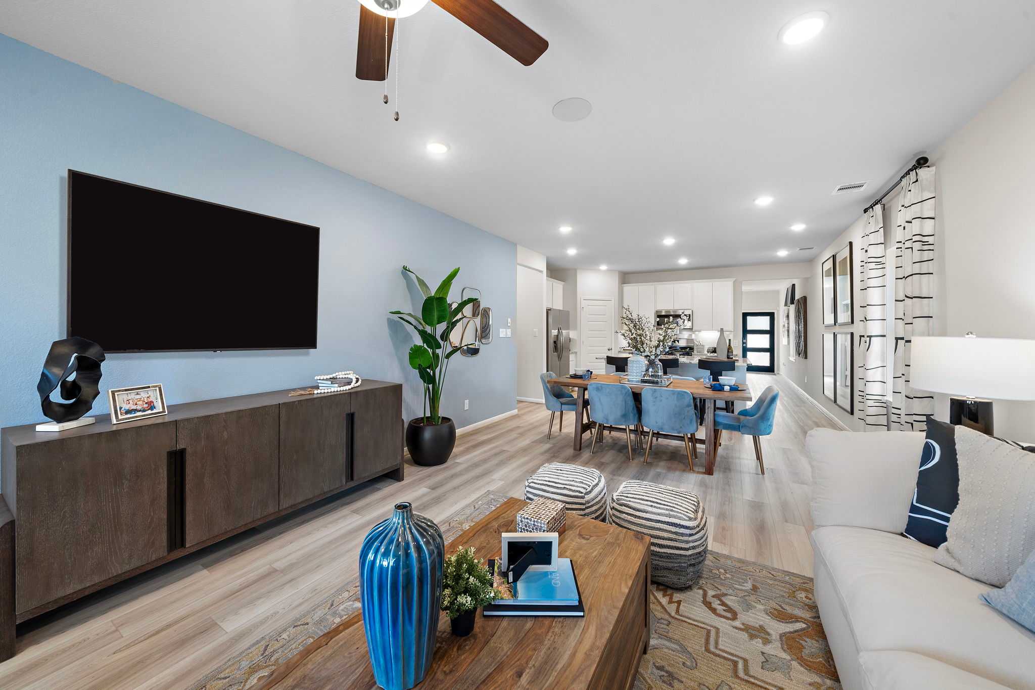 Open-concept living and dining room at Lakes at Black Oak in Magnolia Texas with blue accent wall hardwood floors mounted TV and modern furniture