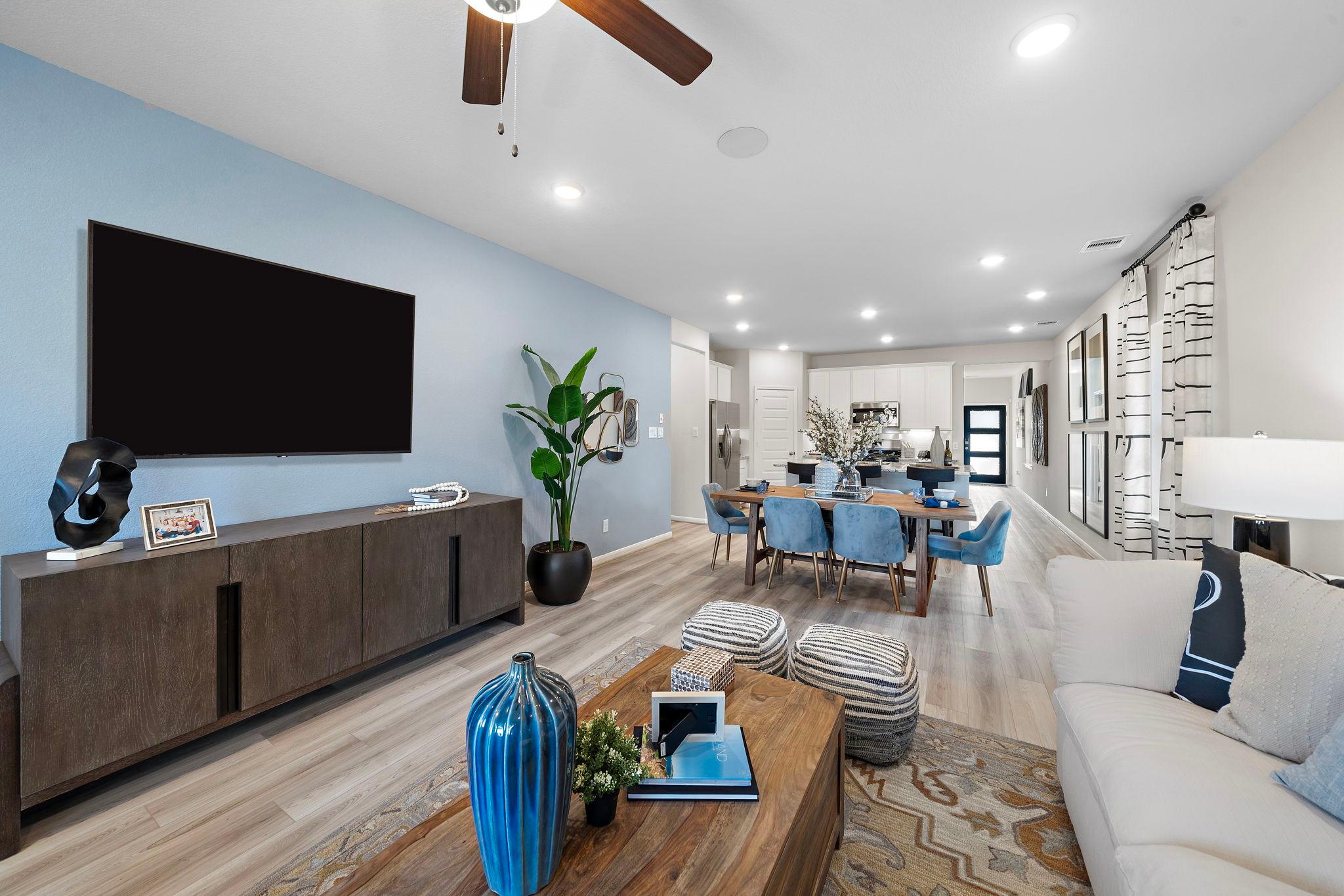 Open-concept living and dining room at Lakes at Black Oak in Magnolia Texas with blue accent wall hardwood floors mounted TV and modern furniture