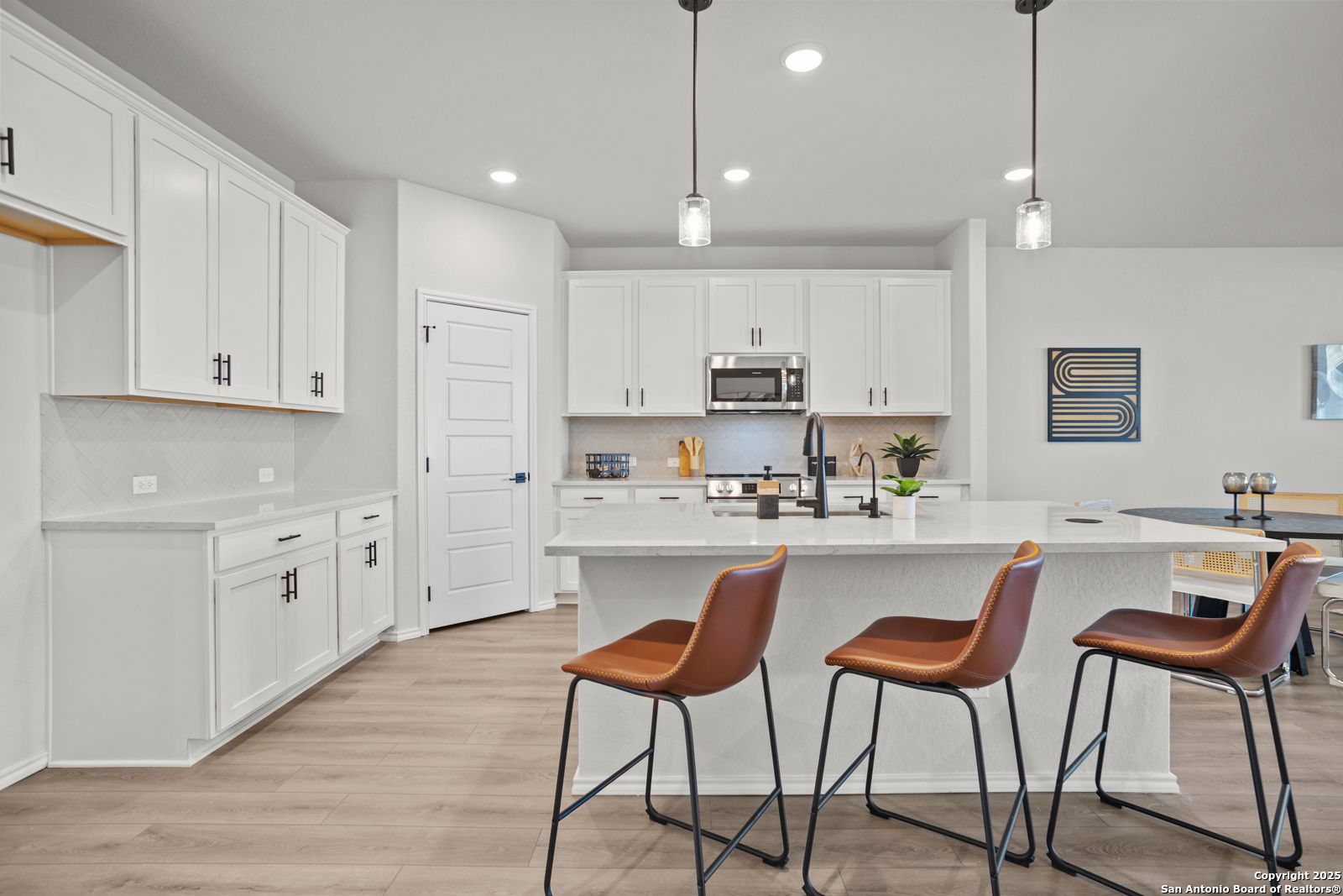 Modern white kitchen with large island, stainless appliances, and pendant lights in Davidson Homes The Douglas C, Seguin, Texas