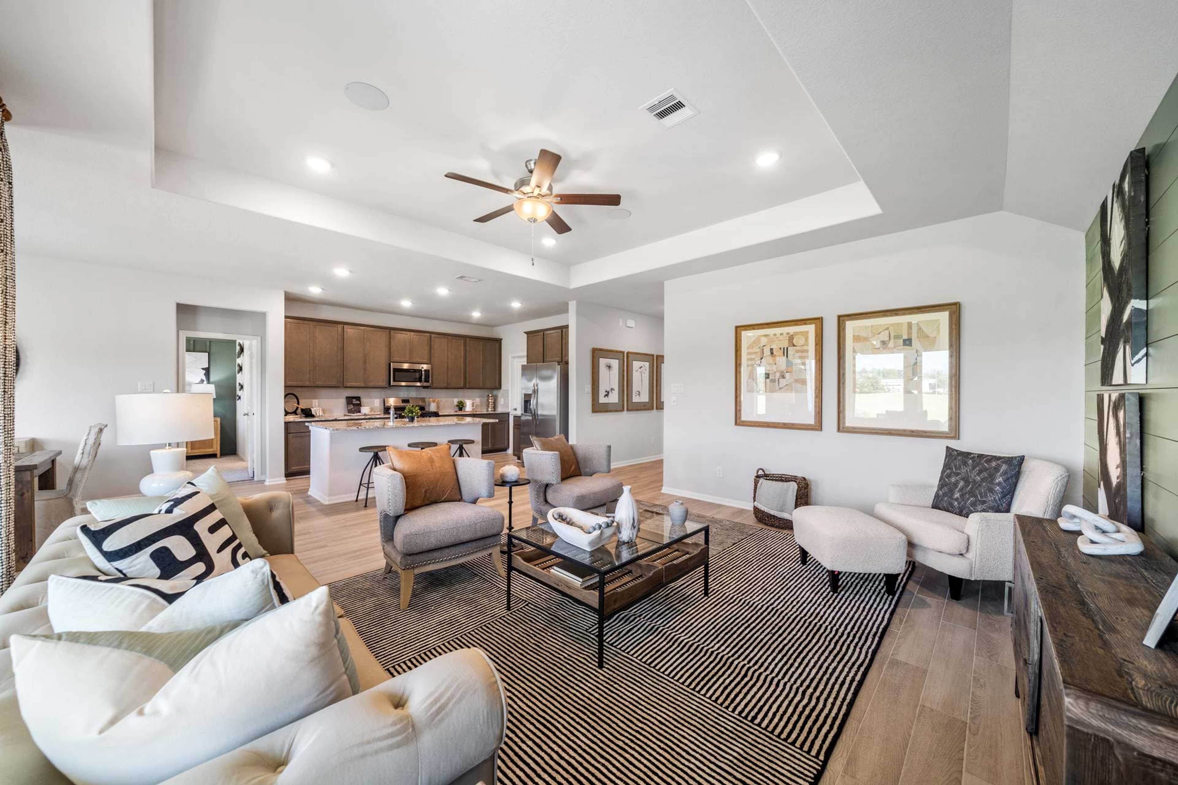 Open-concept living room and kitchen at Windmill Estates in Magnolia Texas featuring hardwood floors, ceiling fan, and modern beige furniture