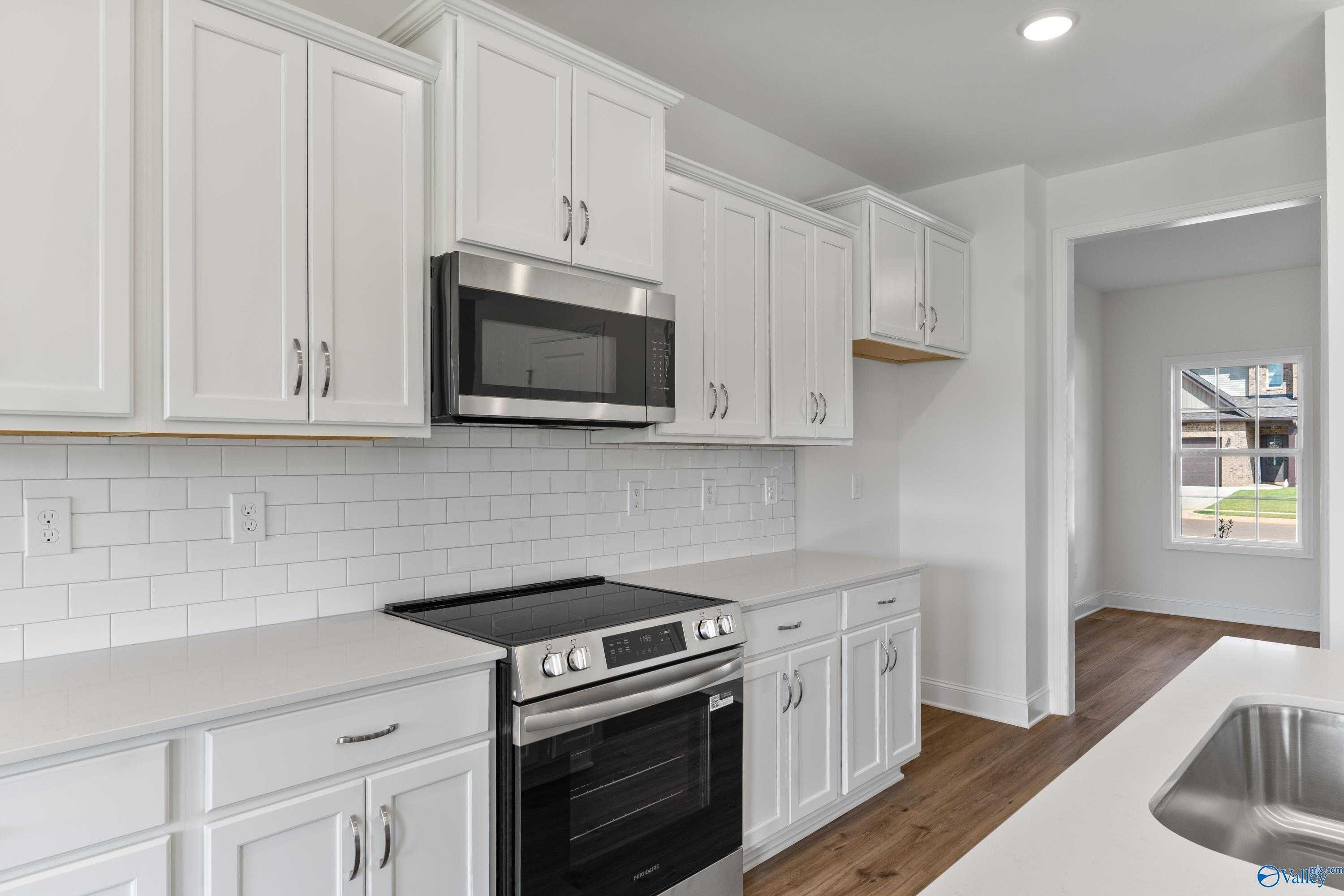 Modern white kitchen with stainless steel microwave, oven, and induction cooktop in Davidson Homes The Shelby A, New Market, AL