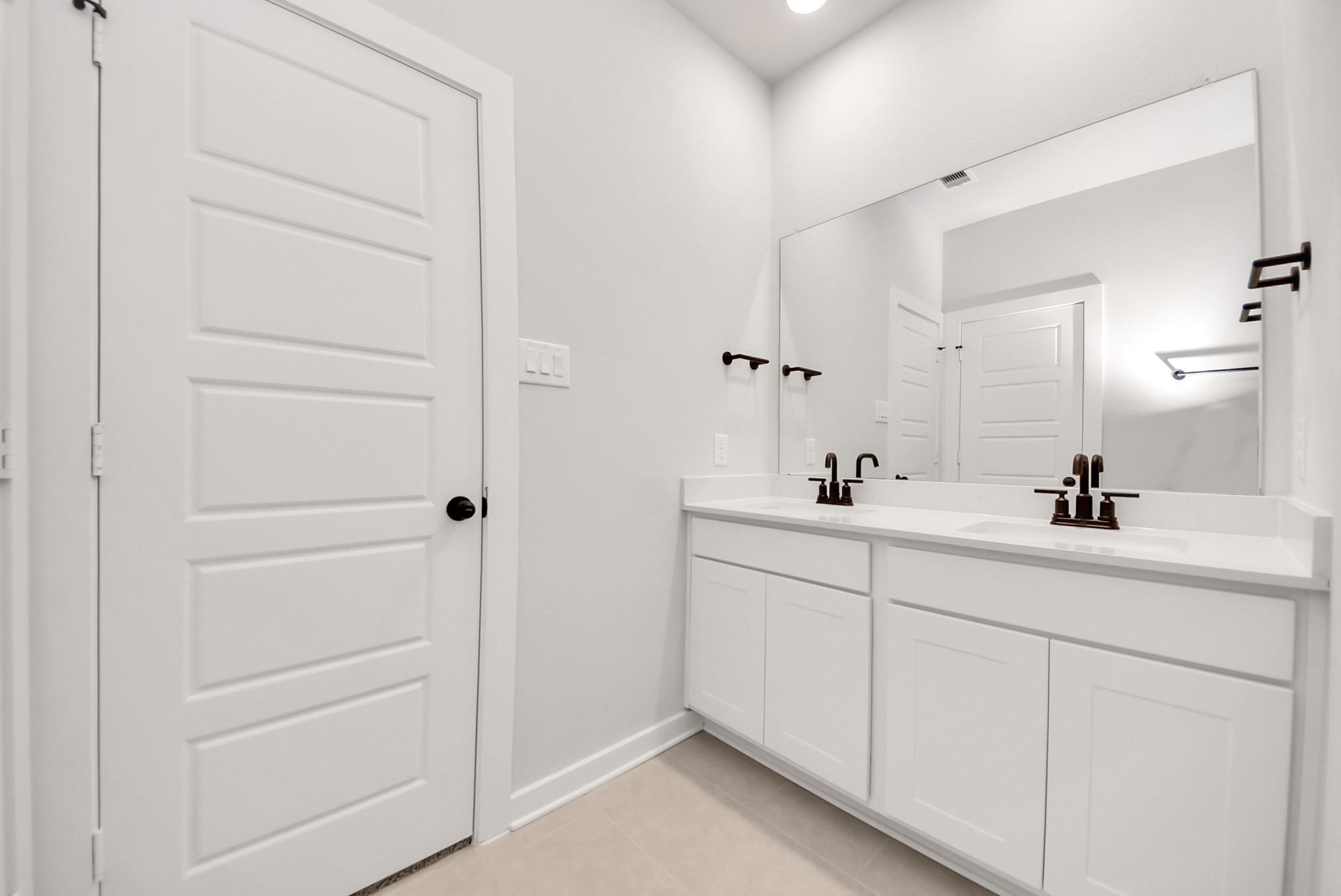 Modern dual-sink bathroom vanity with white cabinets and dark fixtures in The Daphne F home at Sundance Cove, Crosby.