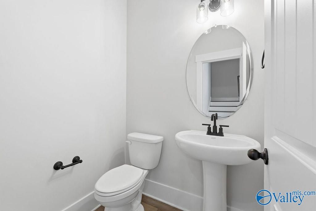 Modern powder room featuring white pedestal sink, round mirror, toilet in Davidson Homes The Rockford, Hartselle, Alabama