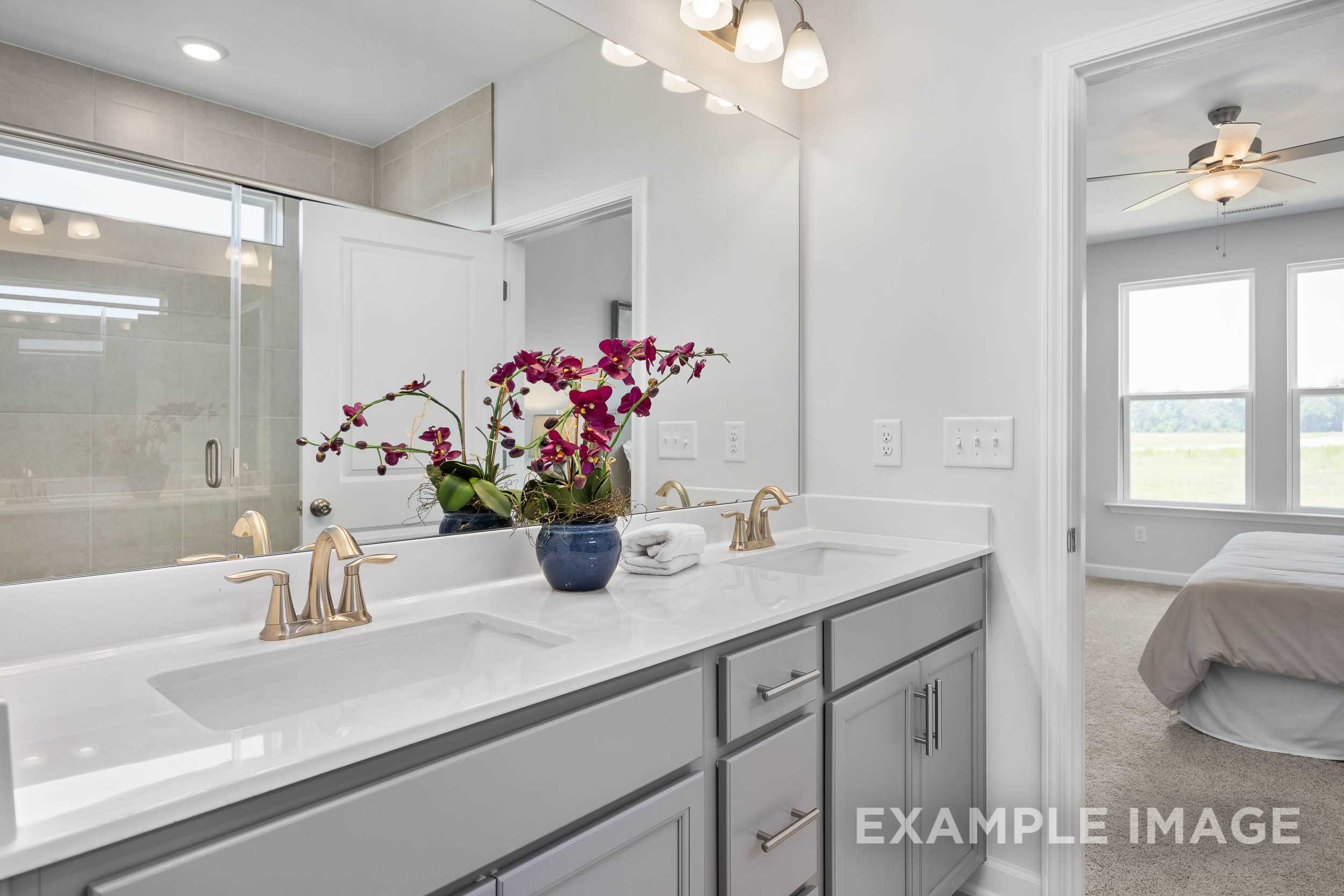 Luxurious master bathroom in The Daphne C featuring double gray vanity, orchids, glass shower, and bedroom view
