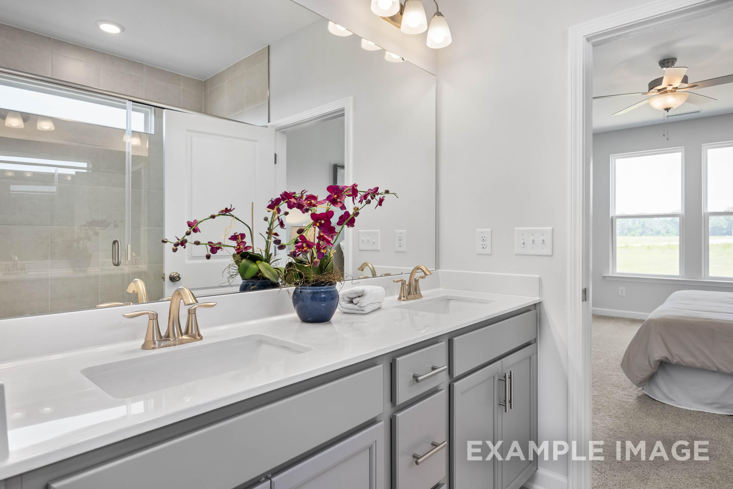 Luxurious master bathroom in The Daphne C featuring double gray vanity, orchids, glass shower, and bedroom view
