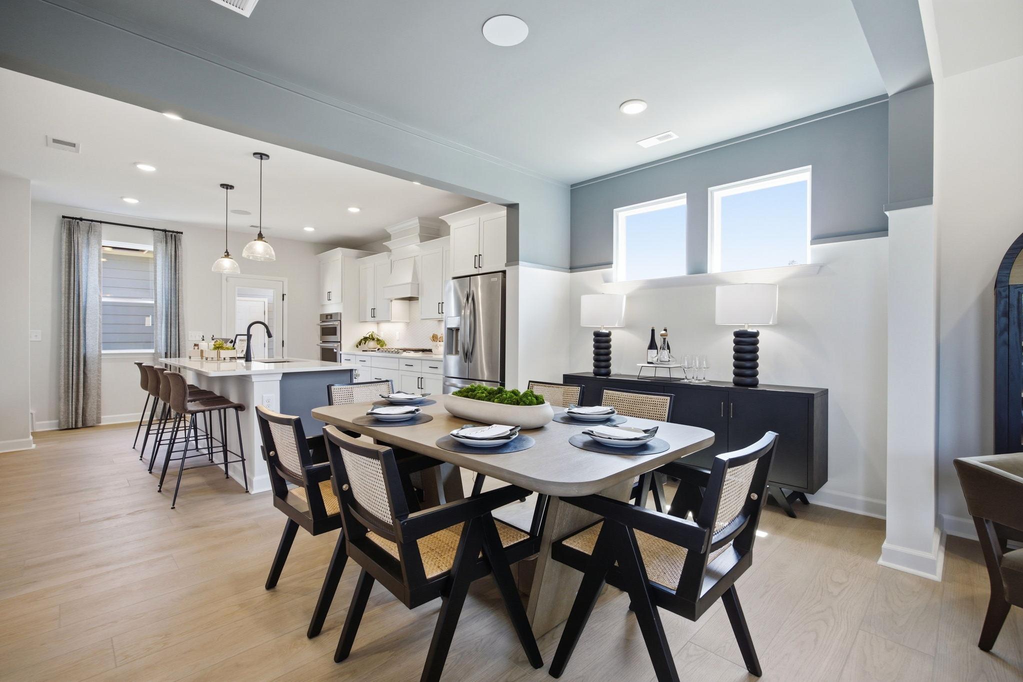 Open-concept dining area and kitchen in The Burke C design featuring wood floors, a large island, and modern decor.