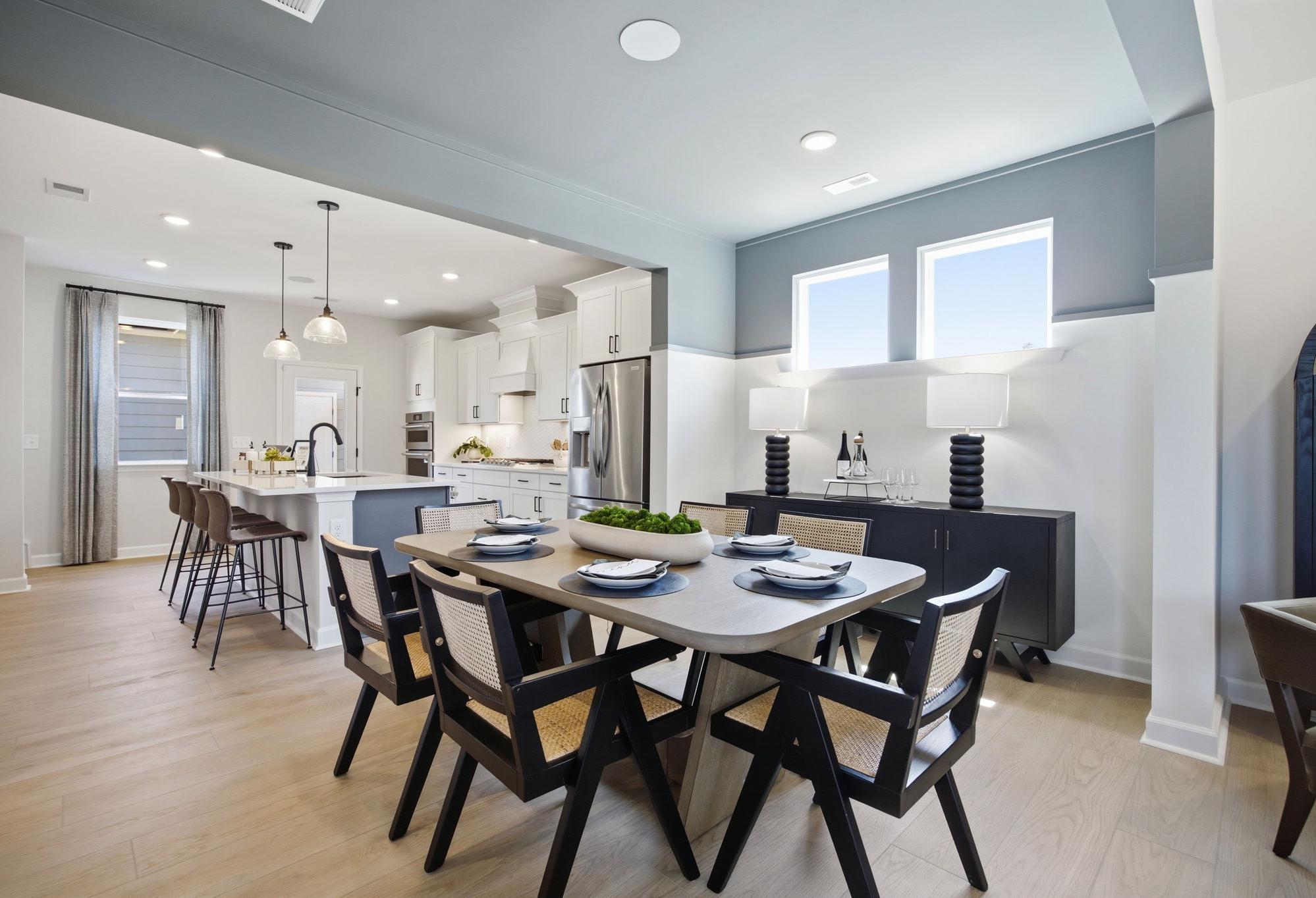 Open-concept dining area and kitchen in The Burke C design featuring wood floors, a large island, and modern decor.