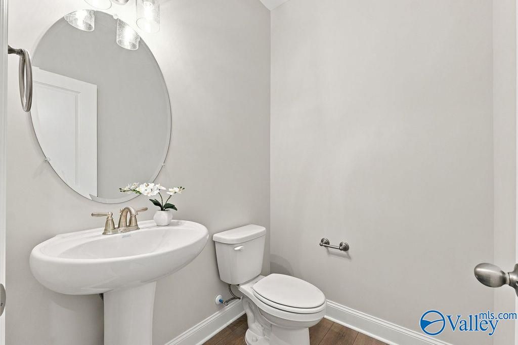 Elegant powder room with pedestal sink, round mirror, and brushed nickel fixtures in Davidson Homes The Harrison, Hartselle, Alabama