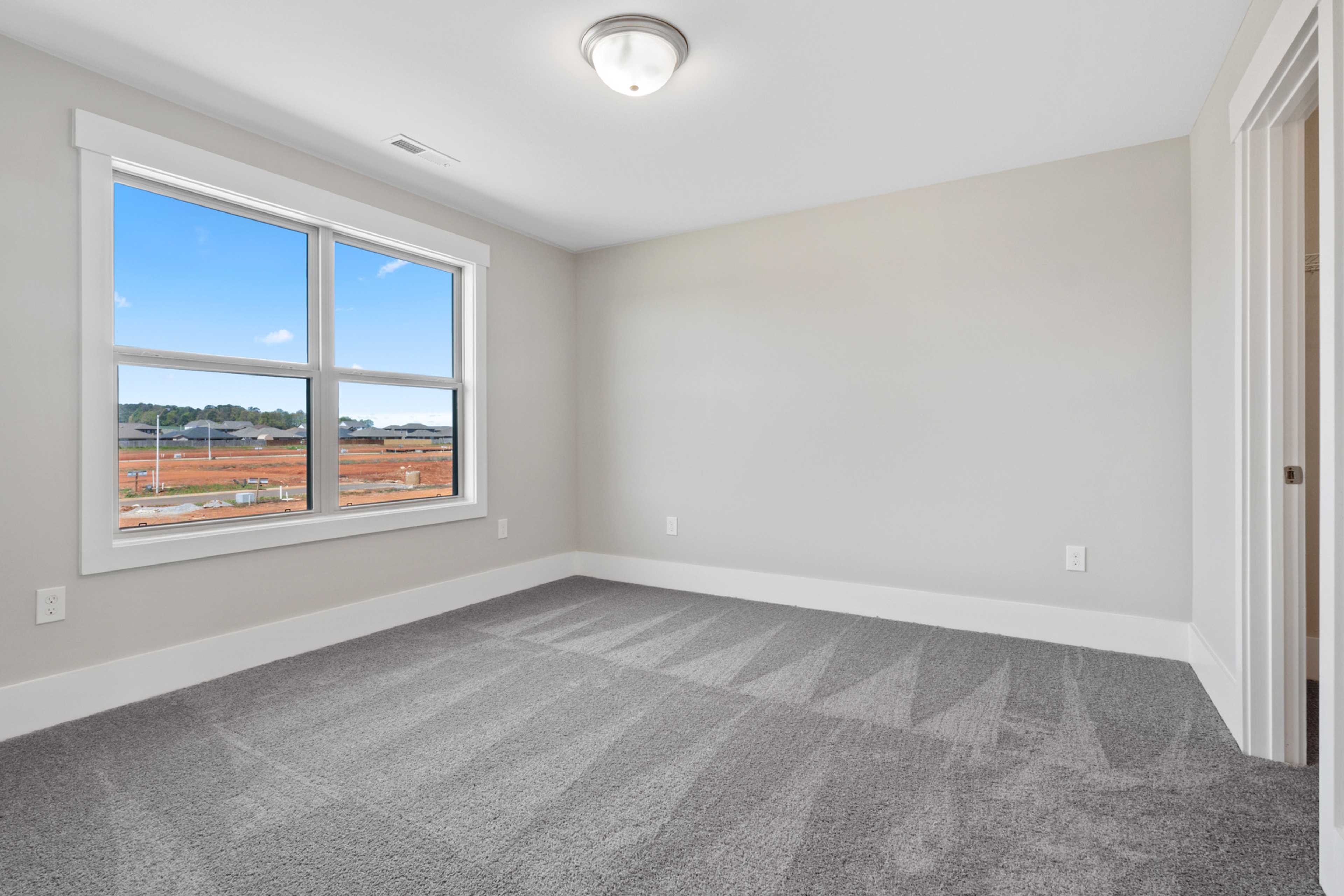 Spacious empty bedroom at Little Burwell Estates in Harvest Alabama with gray carpet, large windows and neutral walls