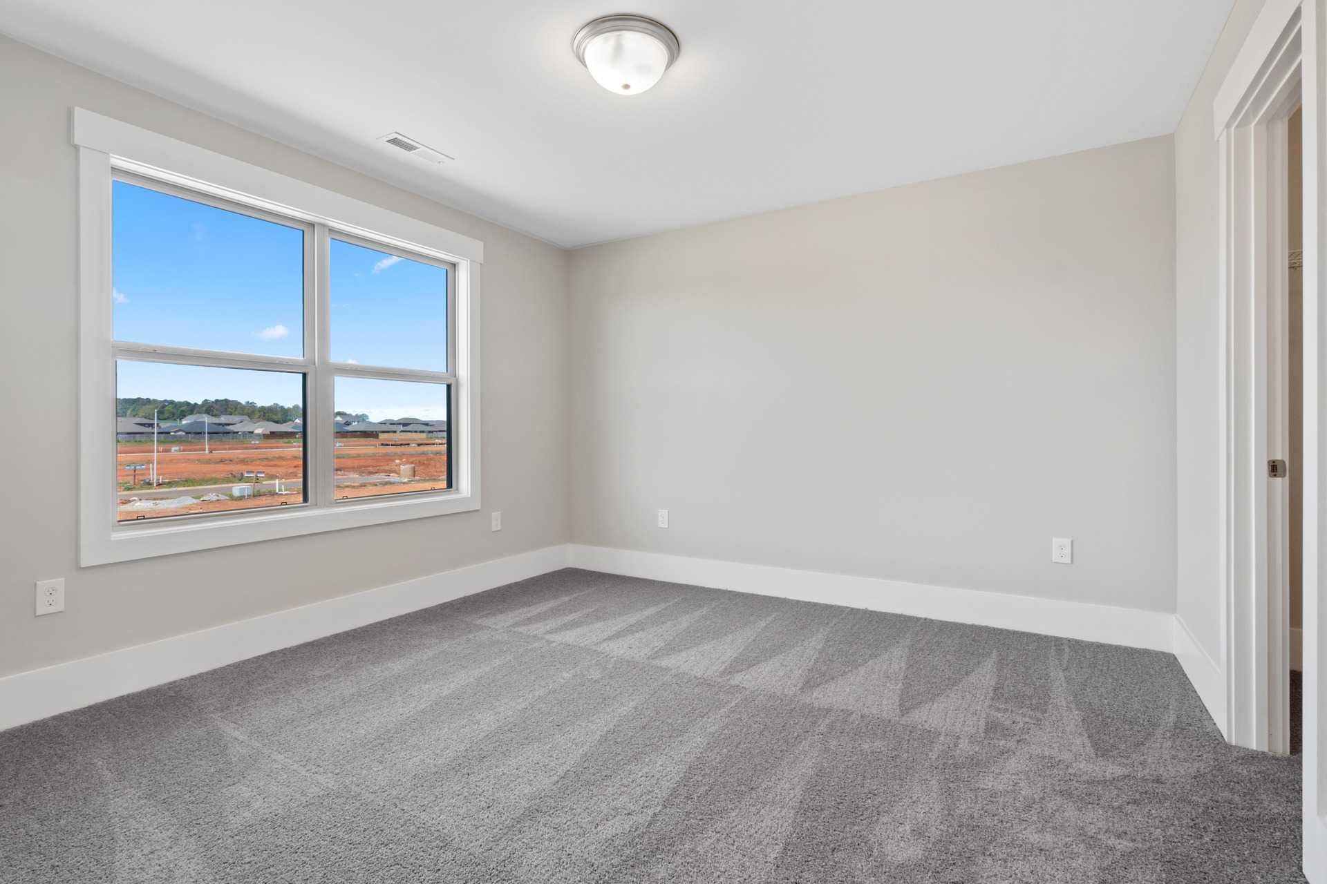 Spacious empty bedroom at Little Burwell Estates in Harvest Alabama with gray carpet, large windows and neutral walls