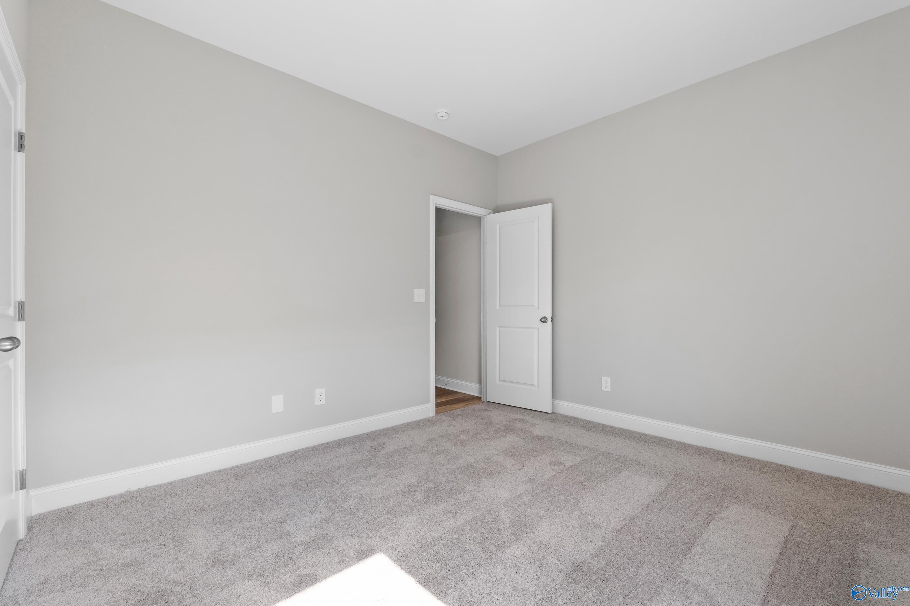 Empty bedroom with light gray walls, white trim, and carpet floor in Davidson Homes The Everett B, Toney, Alabama