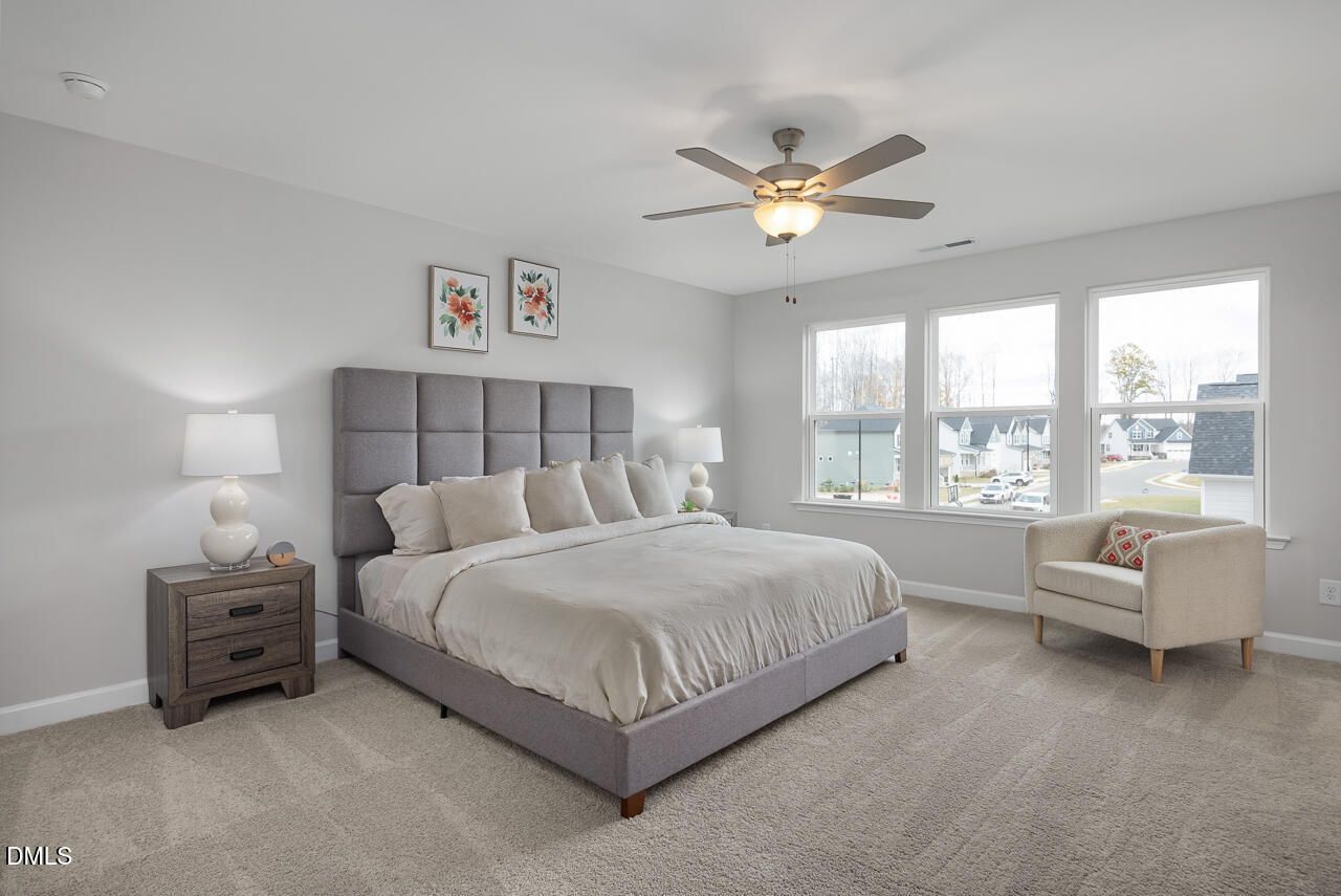 Spacious master bedroom with gray upholstered headboard, white linens, ceiling fan, and large windows in Davidson Homes The Chestnut B, Lillington, NC