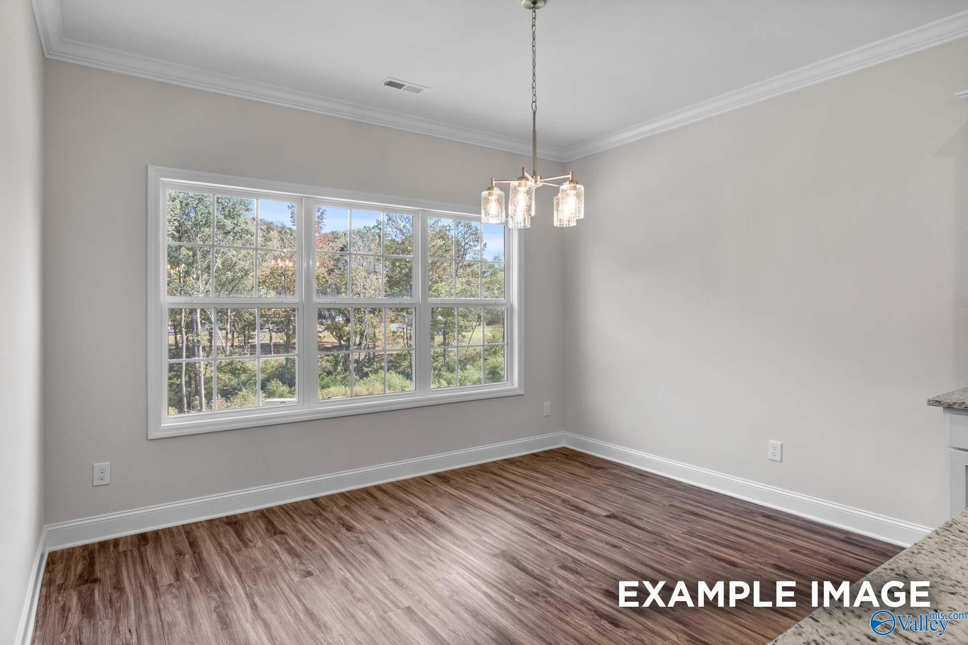 Bright dining area with large triple windows overlooking wooded greenery, hardwood floors, neutral walls, and chandelier in Davidson Homes Montgomery C, Harvest AL