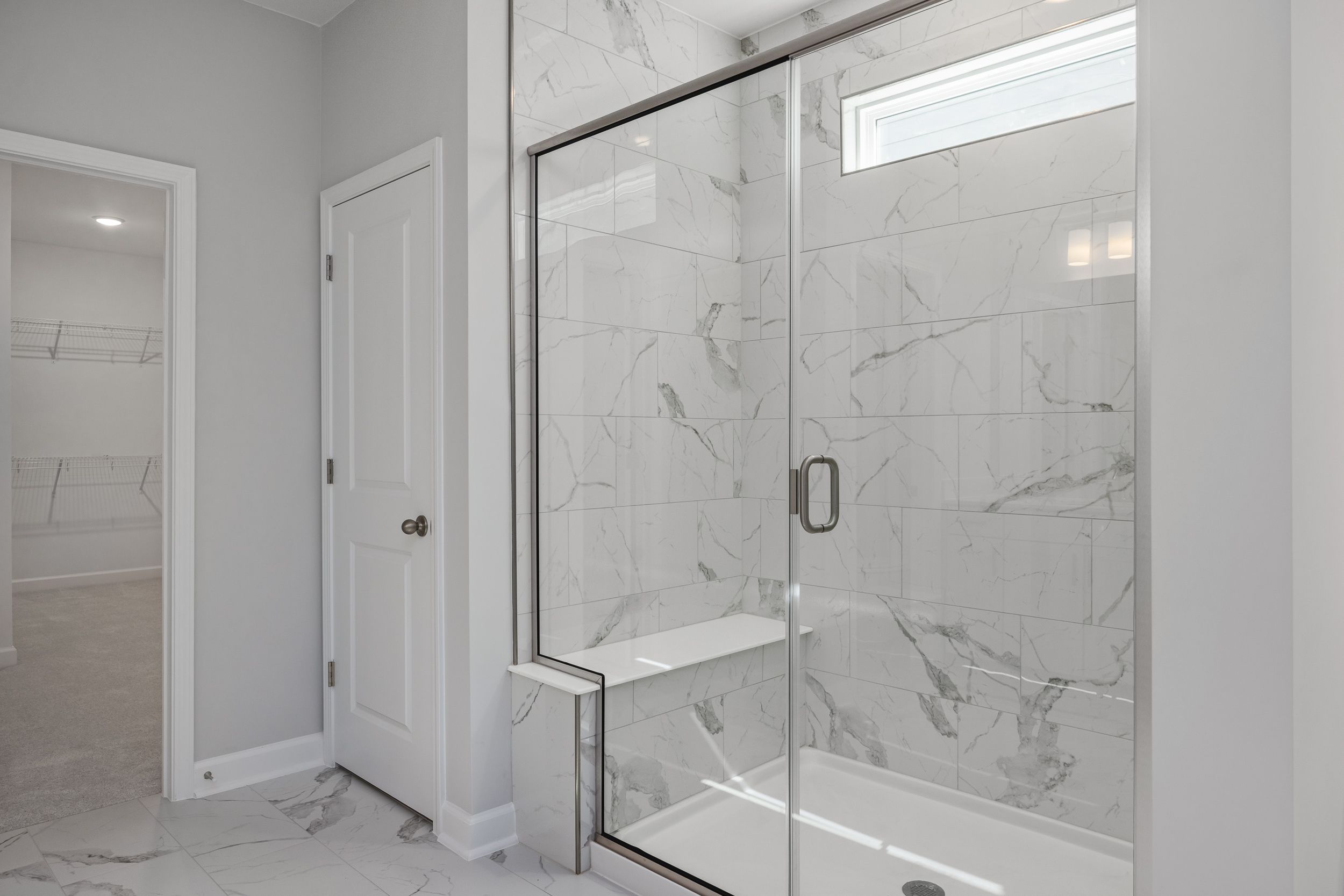 Modern frameless glass shower with marble tiles and built-in bench in The Aspen C master bathroom