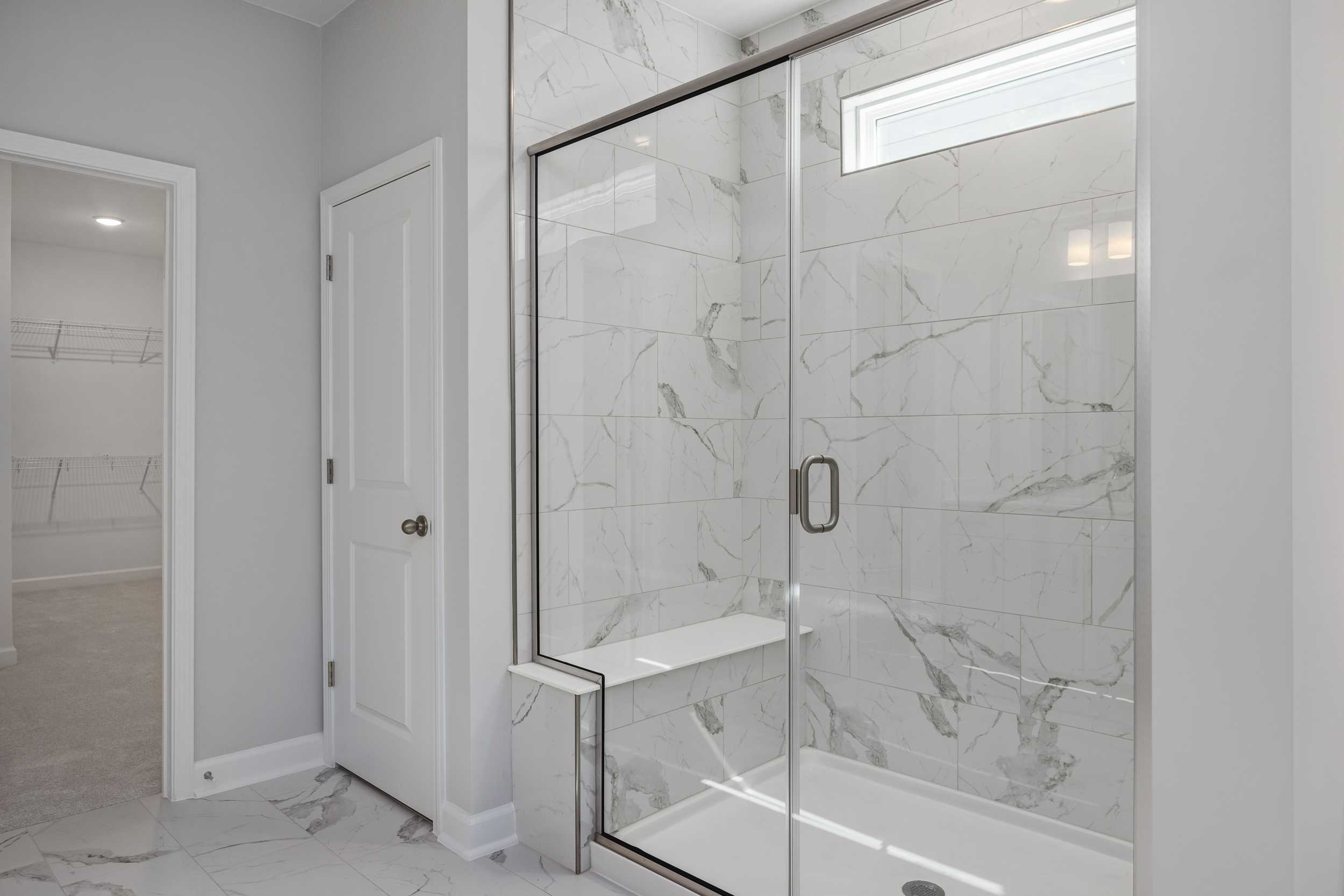Modern frameless glass shower with marble tiles and built-in bench in The Aspen C master bathroom